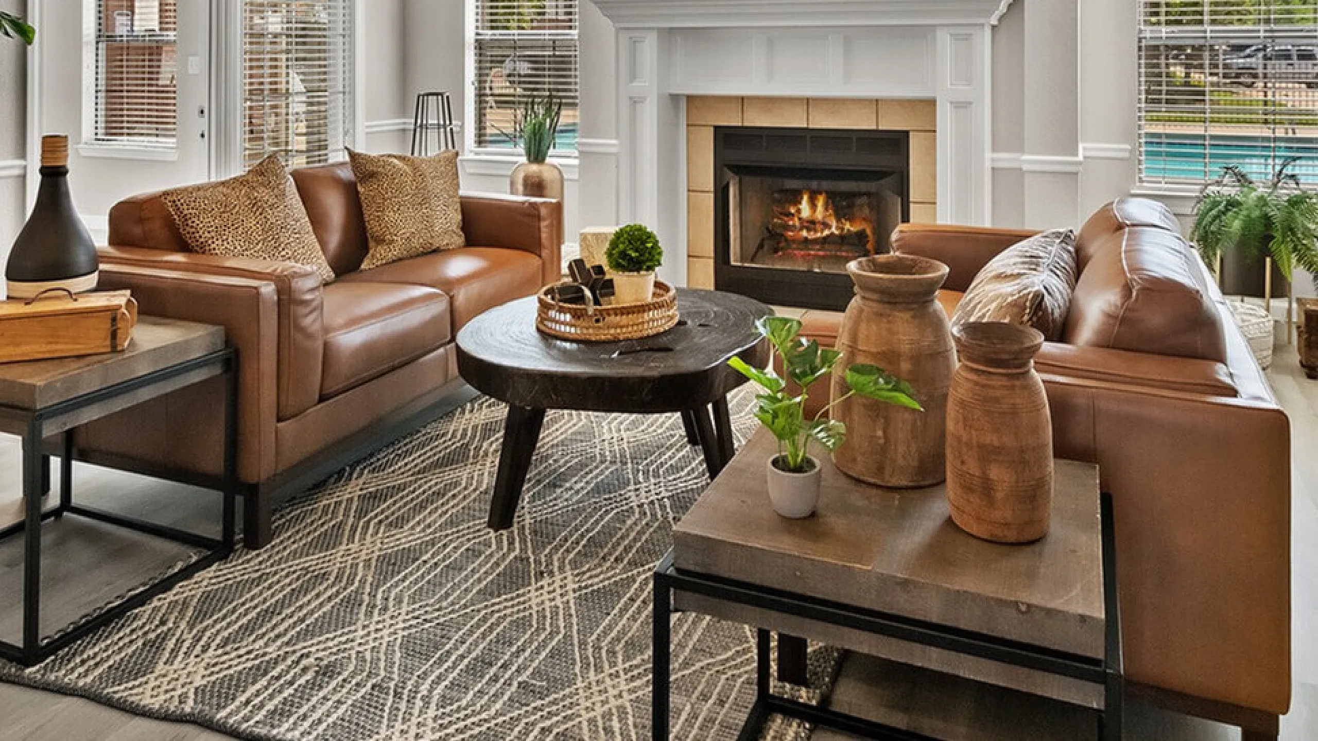 Elegant living room with leather sofas, modern decor, and a cozy fireplace, featuring large windows with scenic views and natural light.