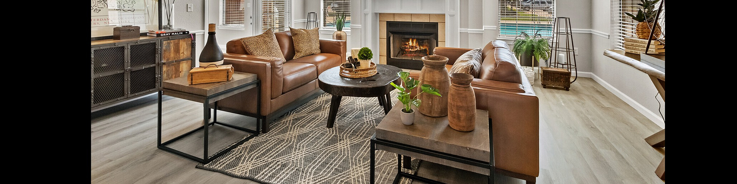 Inviting living room with stylish leather sofas, a cozy fireplace, and abundant natural light overlooking a serene outdoor view.