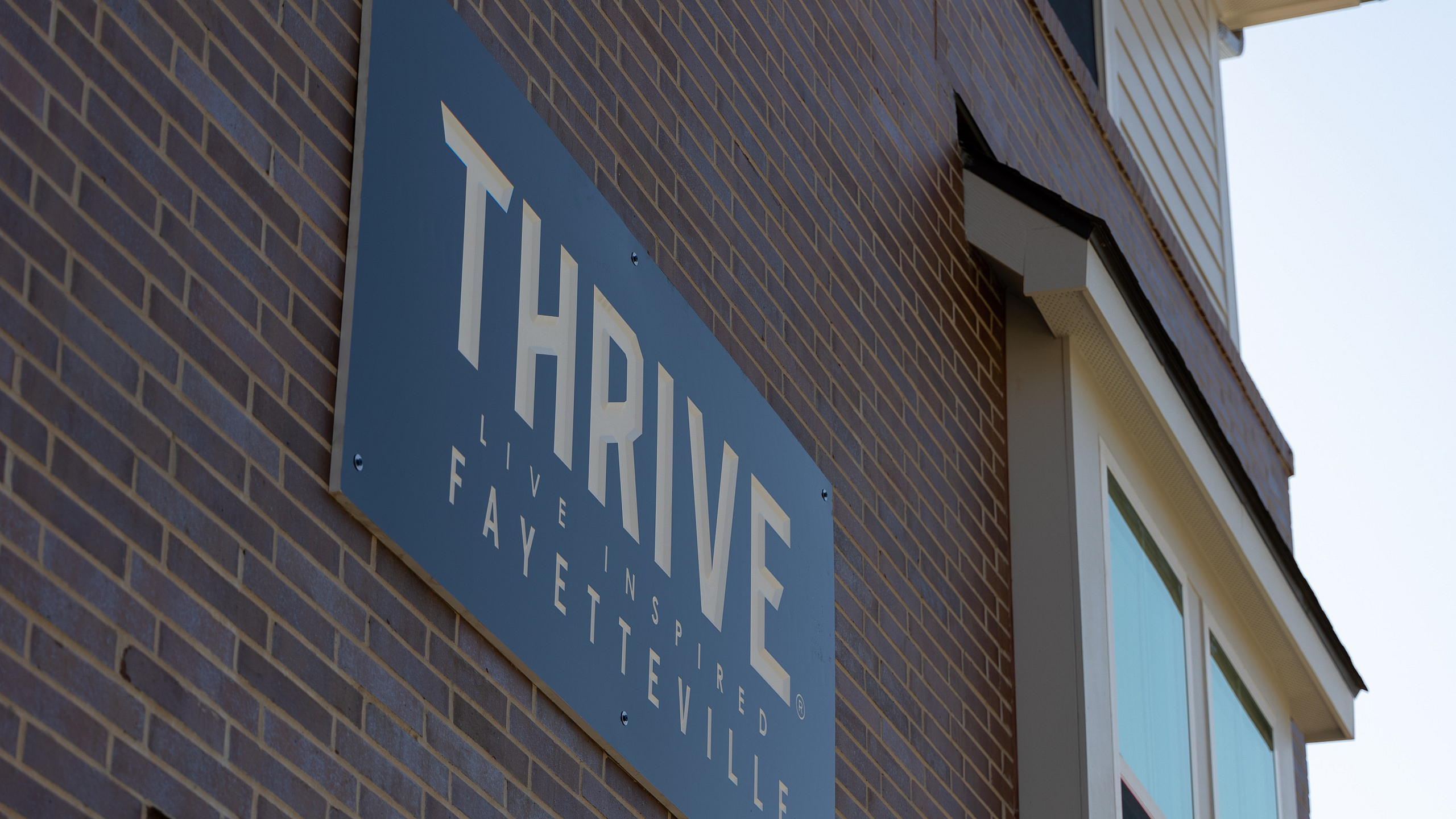 Modern apartment building with stylish 'THRIVE Live Inspired Fayetteville' signage on a brick facade.