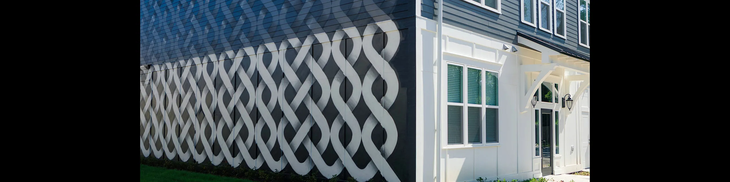 Modern apartment exterior with bold geometric mural design, pristine white accents, and lush green surroundings.