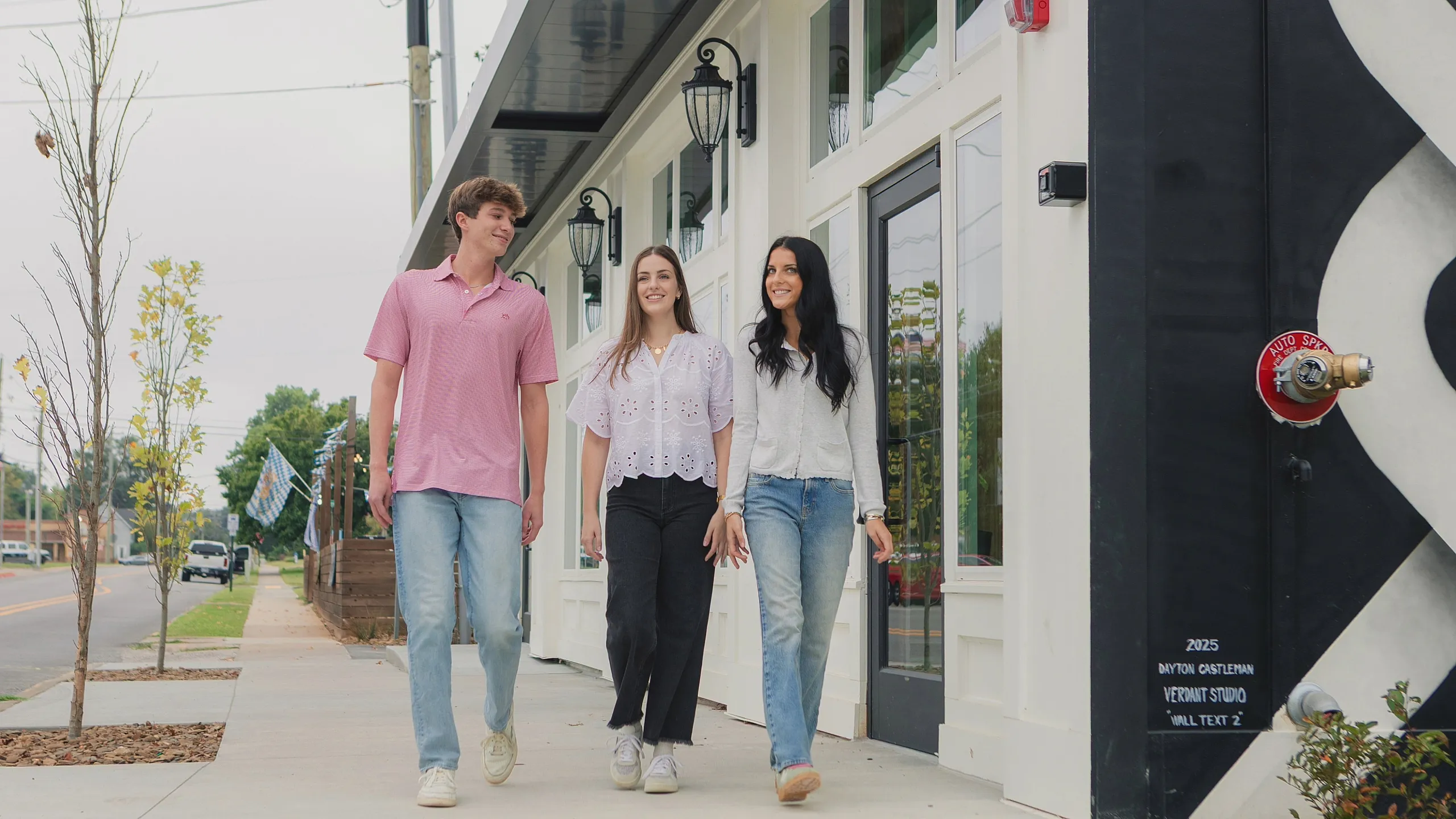 Three friends happily walking on a modern city sidewalk, showcasing a vibrant and welcoming neighborhood.