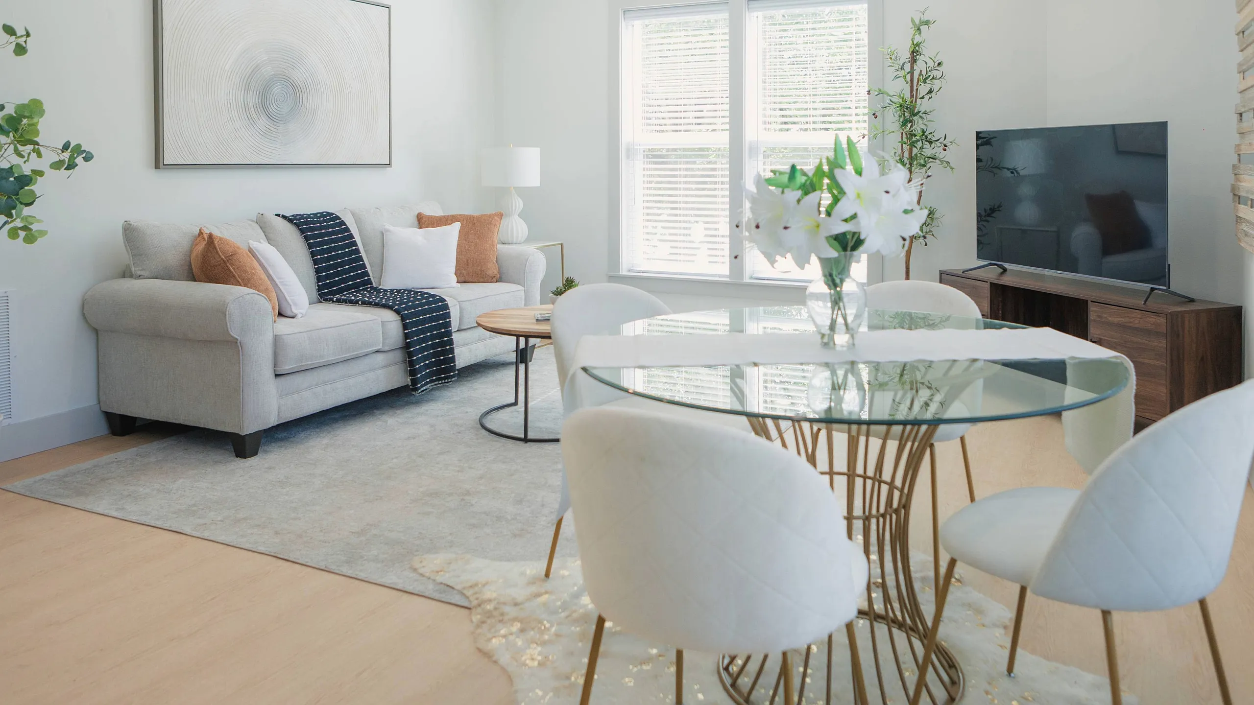 Inviting living room with a cozy gray sofa, stylish glass dining table with elegant chairs, and refreshing natural light streaming through large windows.