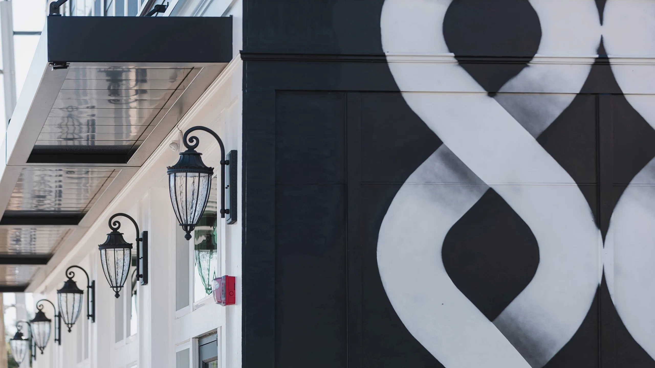 Modern building exterior featuring stylish outdoor lighting and bold black and white geometric mural.
