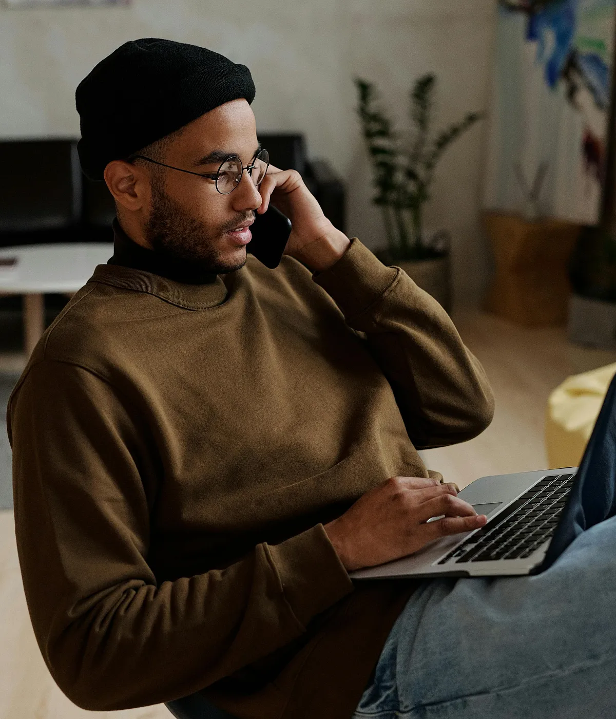 Cozy modern home office setting with a person multitasking on a phone call while using a laptop, surrounded by chic decor and warm lighting.