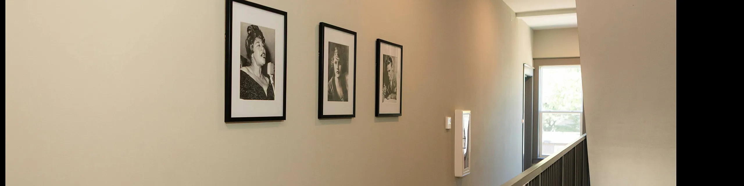 Elegant apartment hallway with stylish framed portraits and natural light from large window.