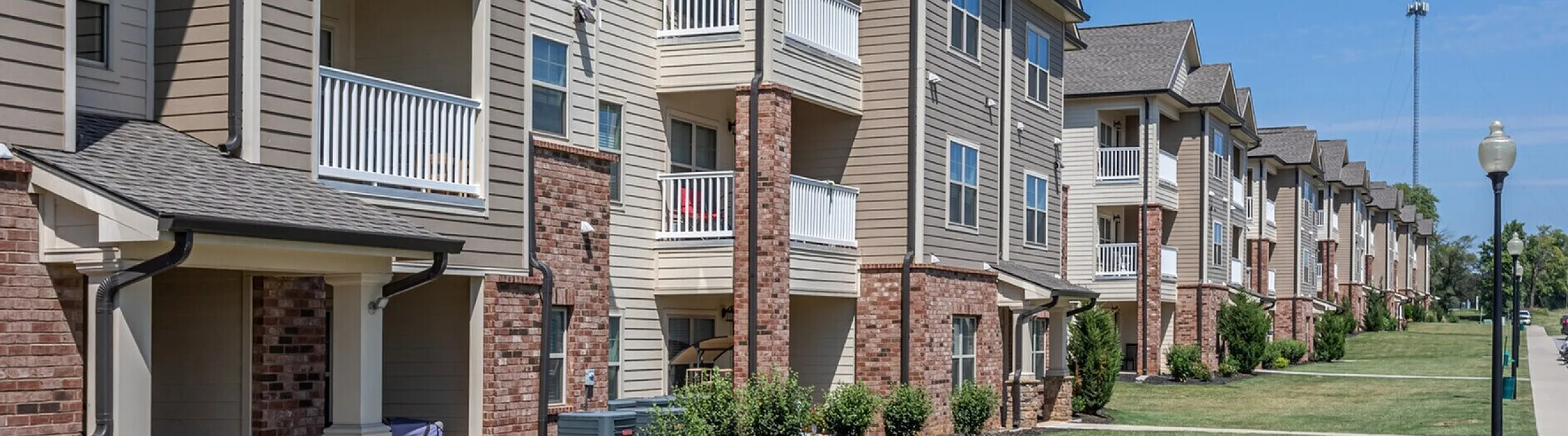 Charming modern apartment complex with stylish brick accents and spacious balconies, offering a serene community feel under a clear blue sky.