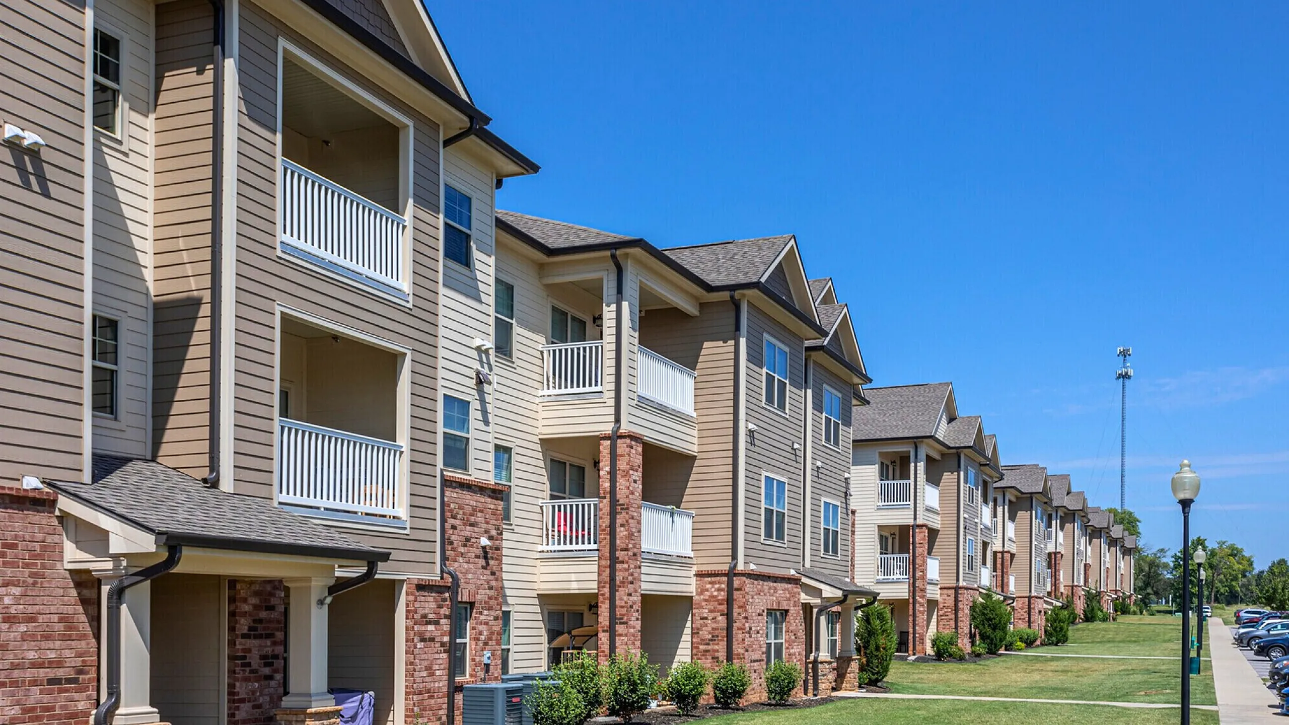 Modern apartment complex with brick accents and private balconies, set against a clear blue sky, offering a blend of luxury and comfort.