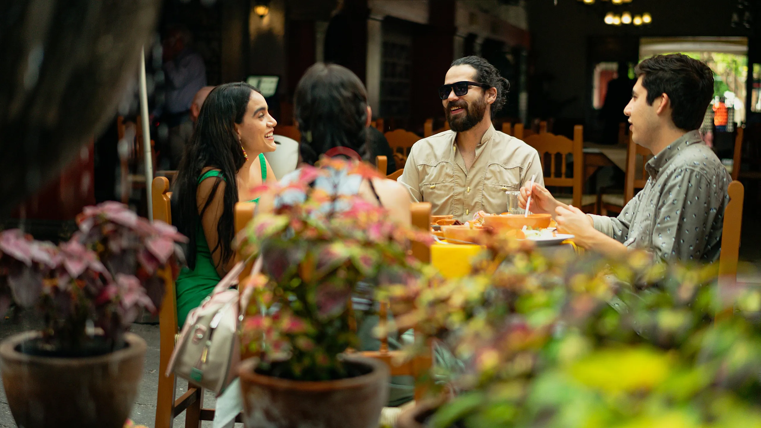 Vibrant scene of friends joyfully dining outdoors, surrounded by lush potted plants, embodying a warm and inviting atmosphere.
