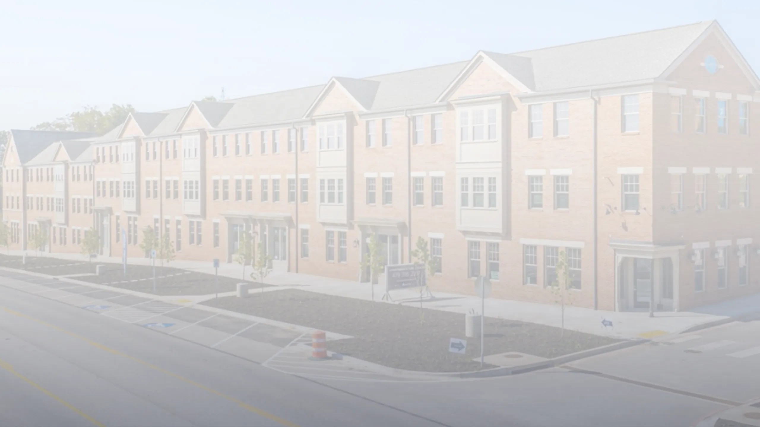 Modern brownstone apartment complex featuring multiple windows and manicured front lawns, set along a well-maintained road in a welcoming neighborhood.