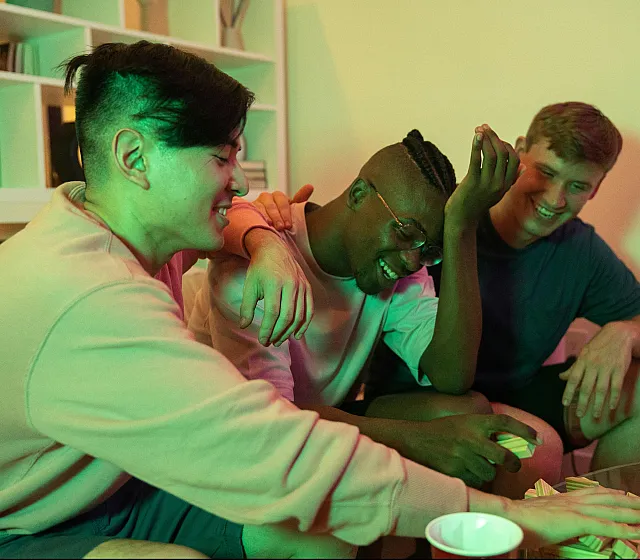 Three friends enjoying a fun game night, laughing together in a cozy living room setting.