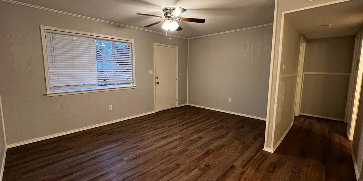 Spacious living room with elegant hardwood floors, neutral gray walls, and a ceiling fan for optimal comfort.