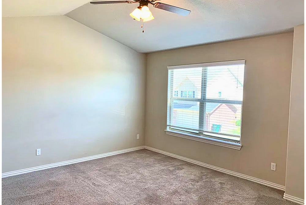 Bright and spacious room with plush carpet, large window, and modern ceiling fan.
