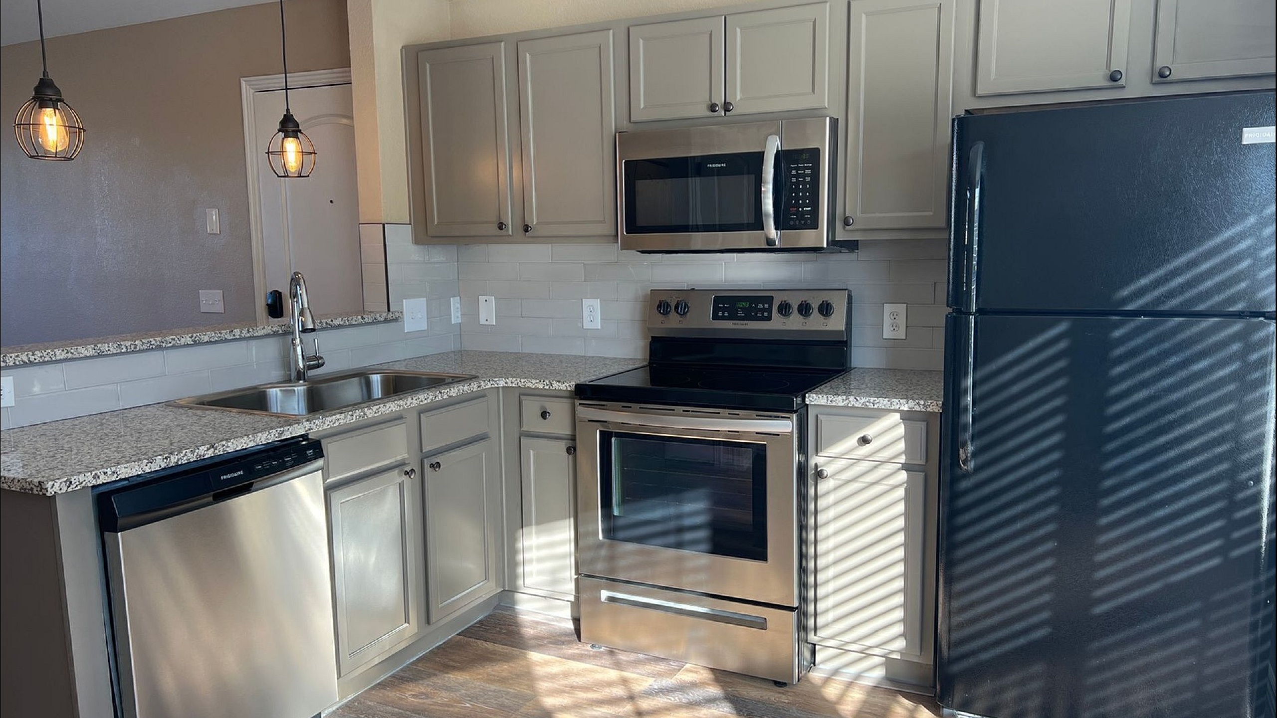 Modern kitchen with sleek stainless steel appliances, elegant granite countertops, and soft grey cabinets accented by warm pendant lighting.