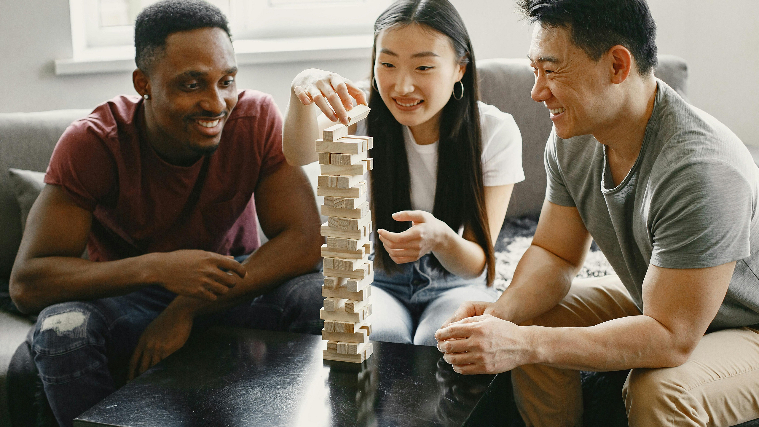 Three friends enjoy a game of Jenga in a cozy, sunlit living room, highlighting the apartment's inviting social space.