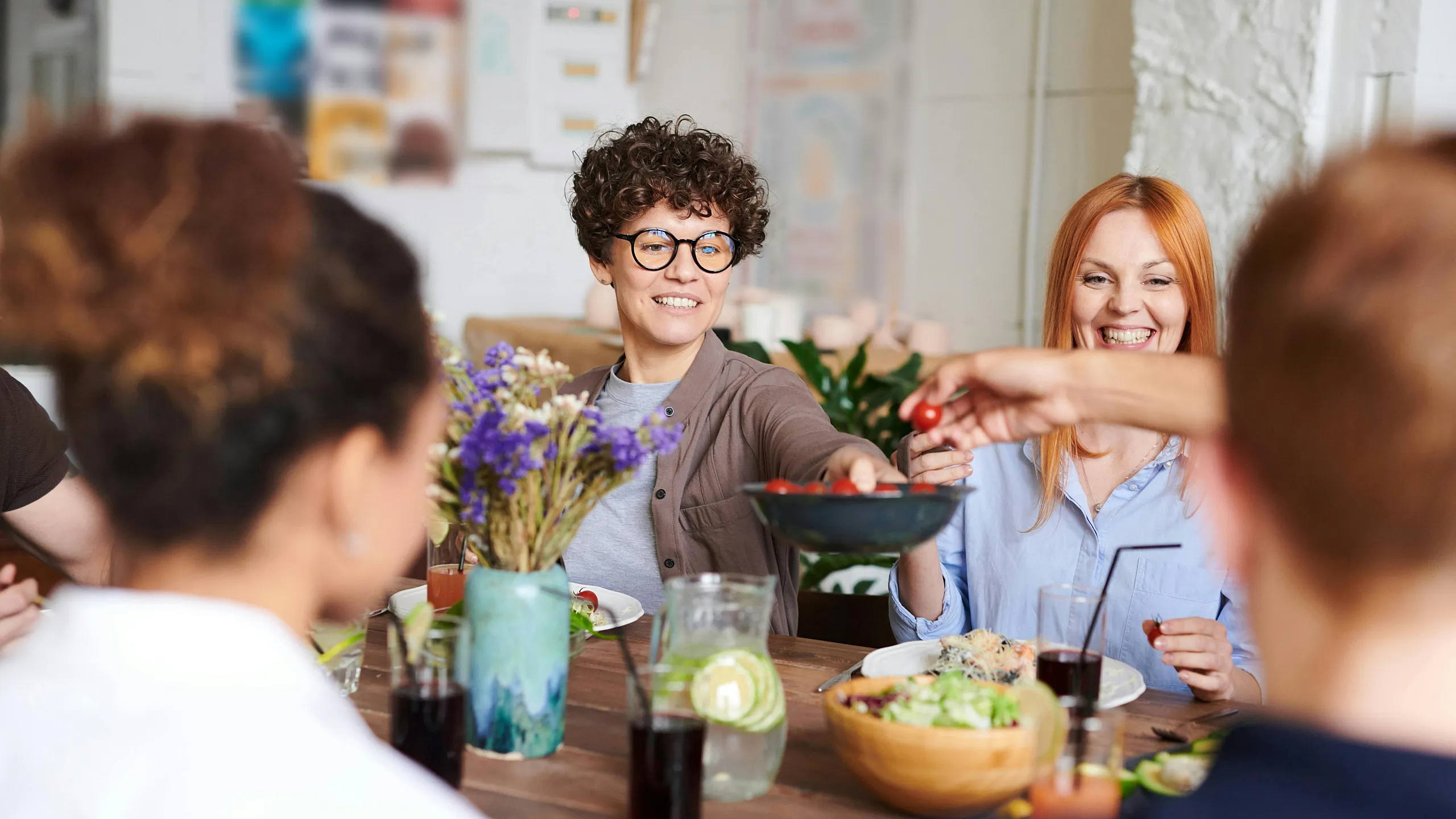 Cheerful group of friends enjoying a meal together in a bright, welcoming dining area with fresh flowers and a variety of delicious dishes.