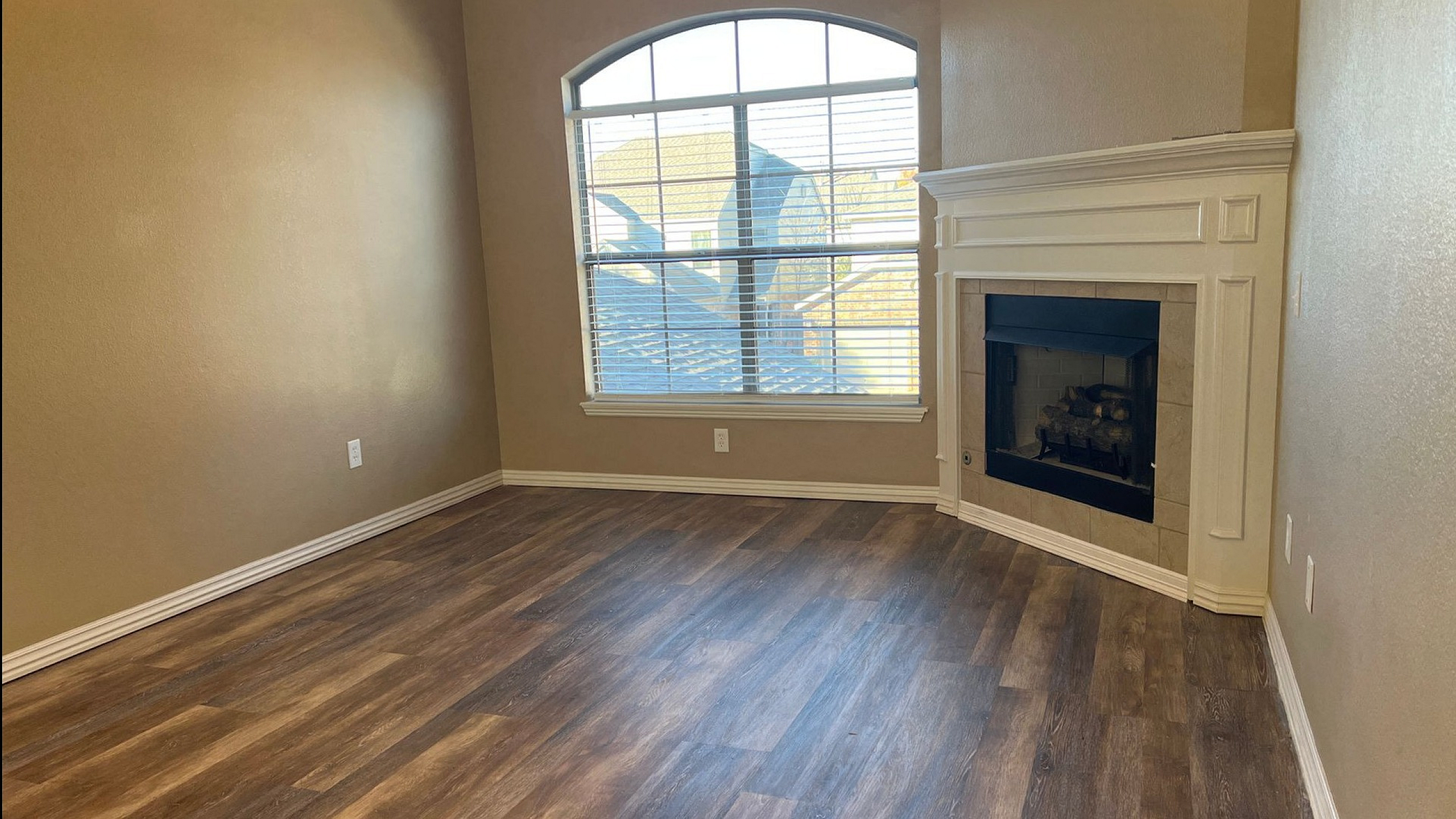 Inviting living room with elegant wood flooring, large arched window, and a charming fireplace for a cozy ambiance.