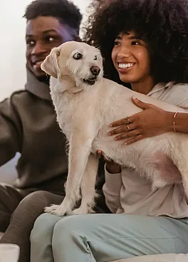Cozy living room with a joyful couple and their fluffy dog relaxing on a comfortable sofa, capturing warmth and happiness.