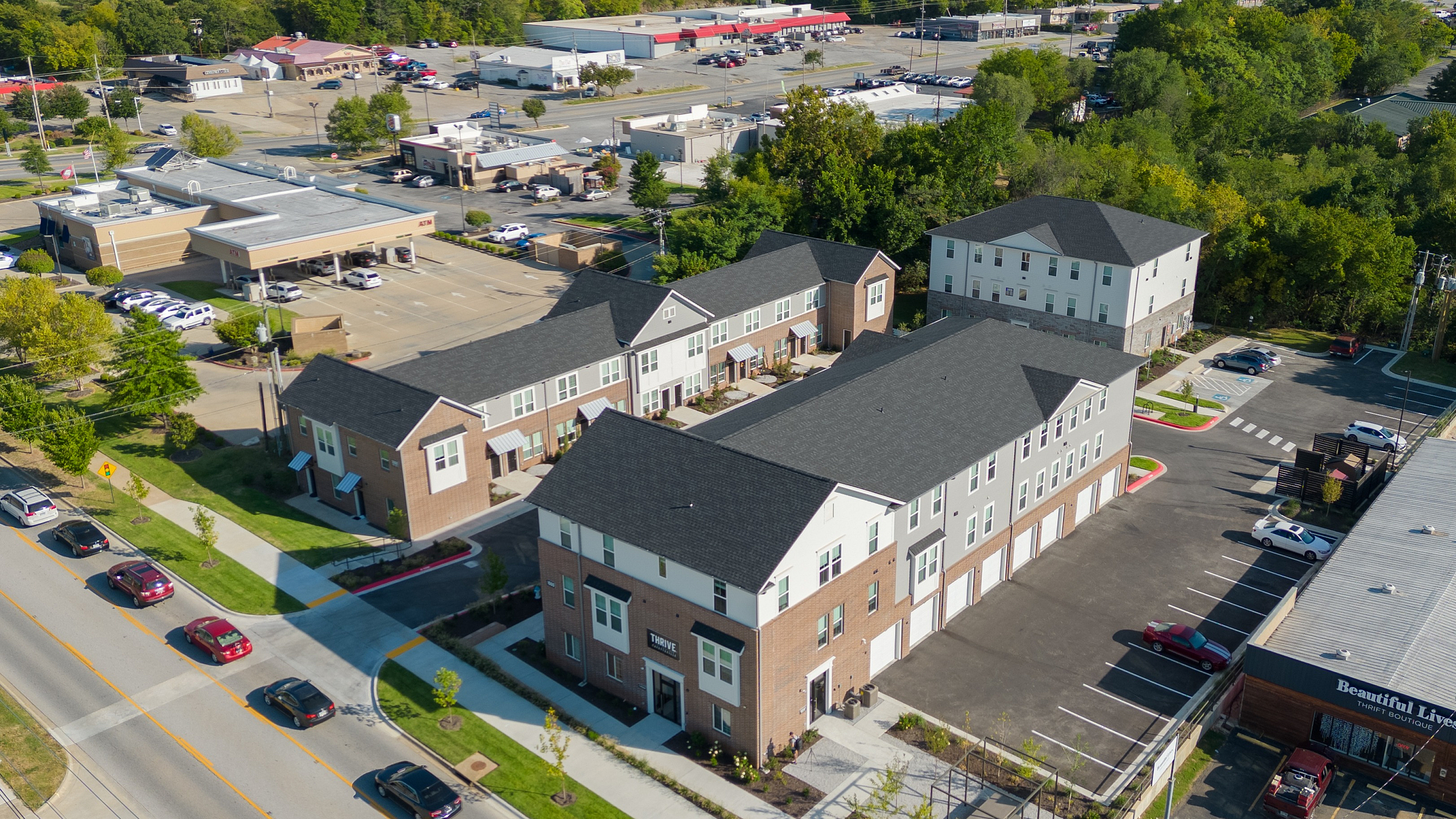 Aerial view of modern townhouses in a vibrant neighborhood, surrounded by lush greenery and a bustling commercial area.
