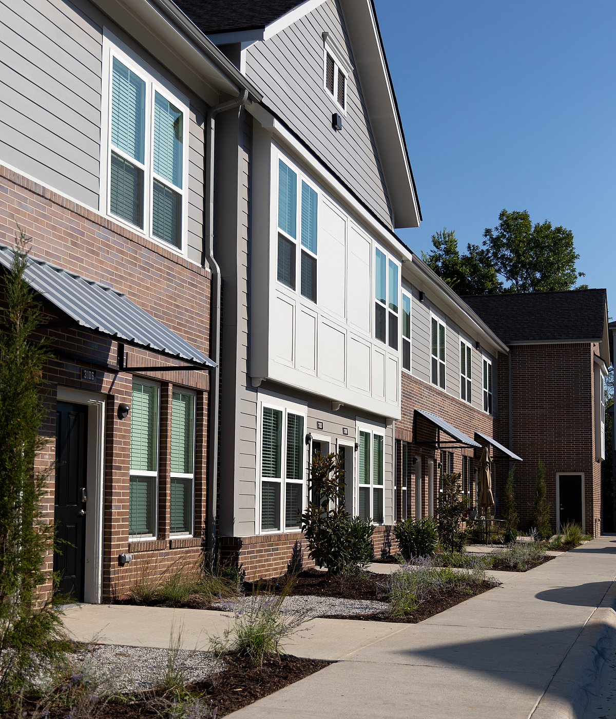Charming modern townhouse with a blend of brick and siding exteriors, featuring large windows and neatly landscaped surroundings.