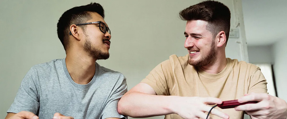 Two friends enjoying a video game, seated comfortably with smiles in a modern, relaxed living space.