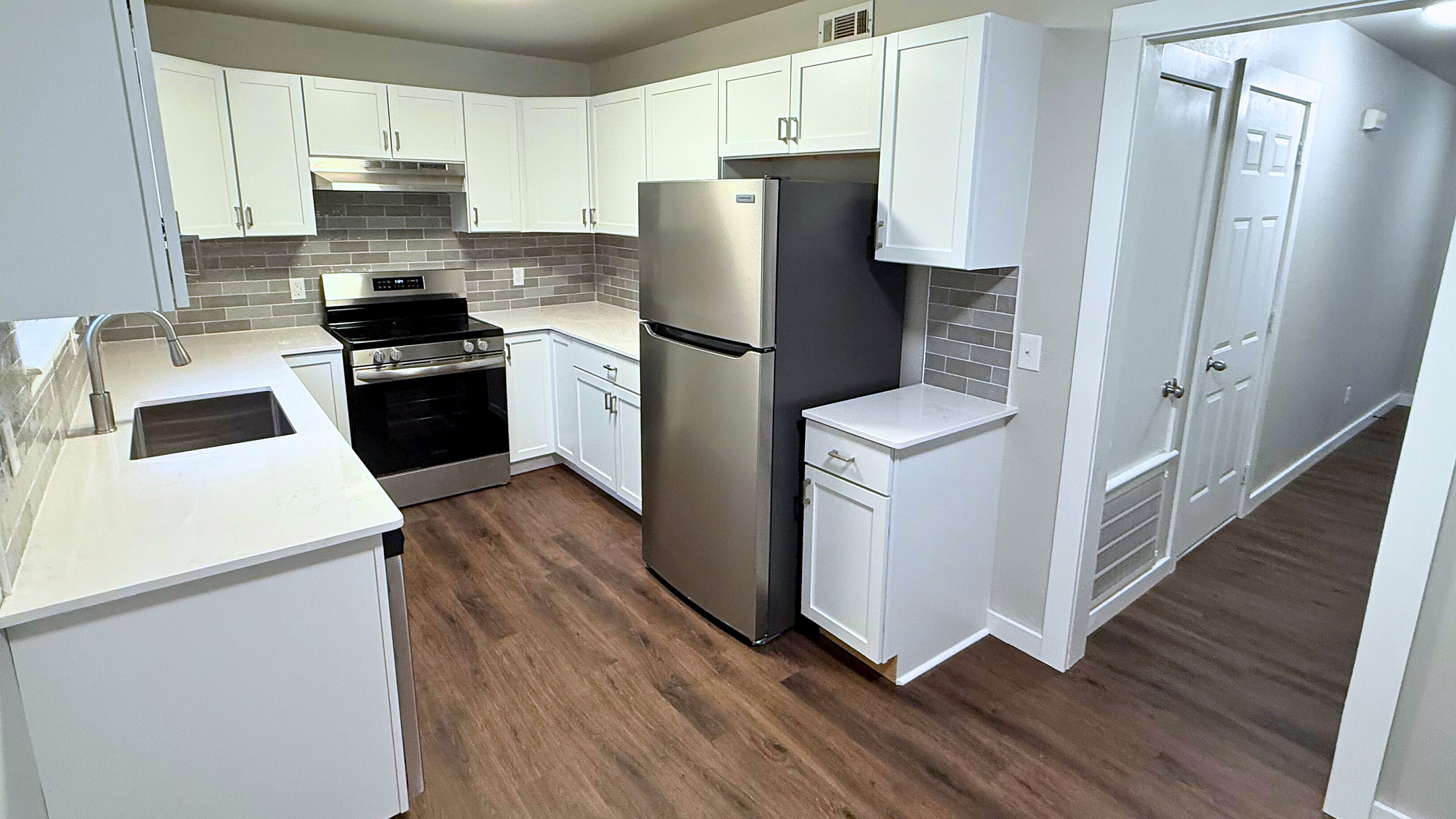 Modern kitchen with sleek stainless steel appliances, elegant white cabinetry, and rich hardwood floors providing a sophisticated and welcoming atmosphere.