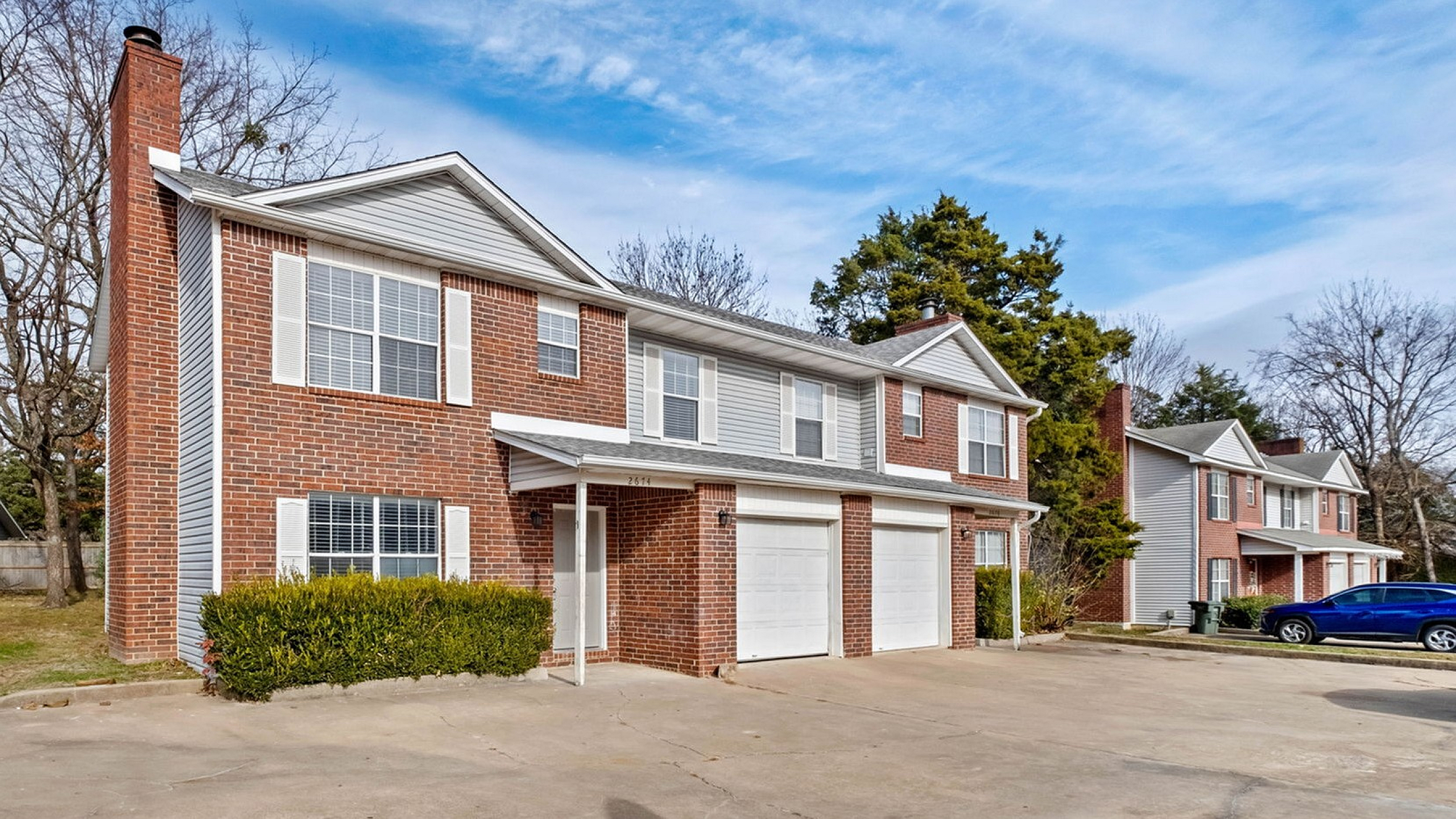 Charming two-story brick townhouse with large windows and attached garage, nestled in a serene suburban neighborhood.