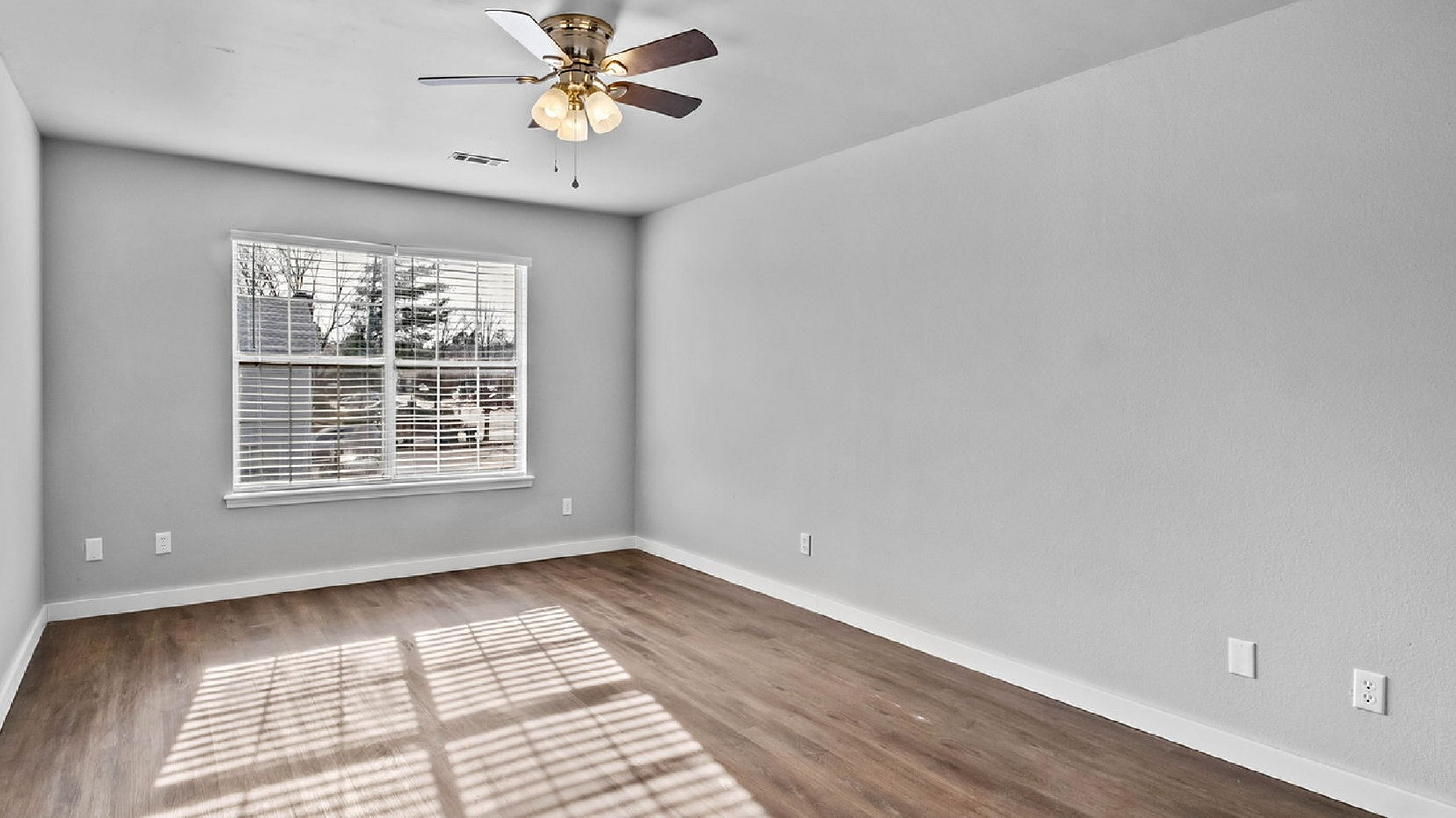 Bright, spacious room with elegant wood flooring, large window for natural light, and stylish ceiling fan.