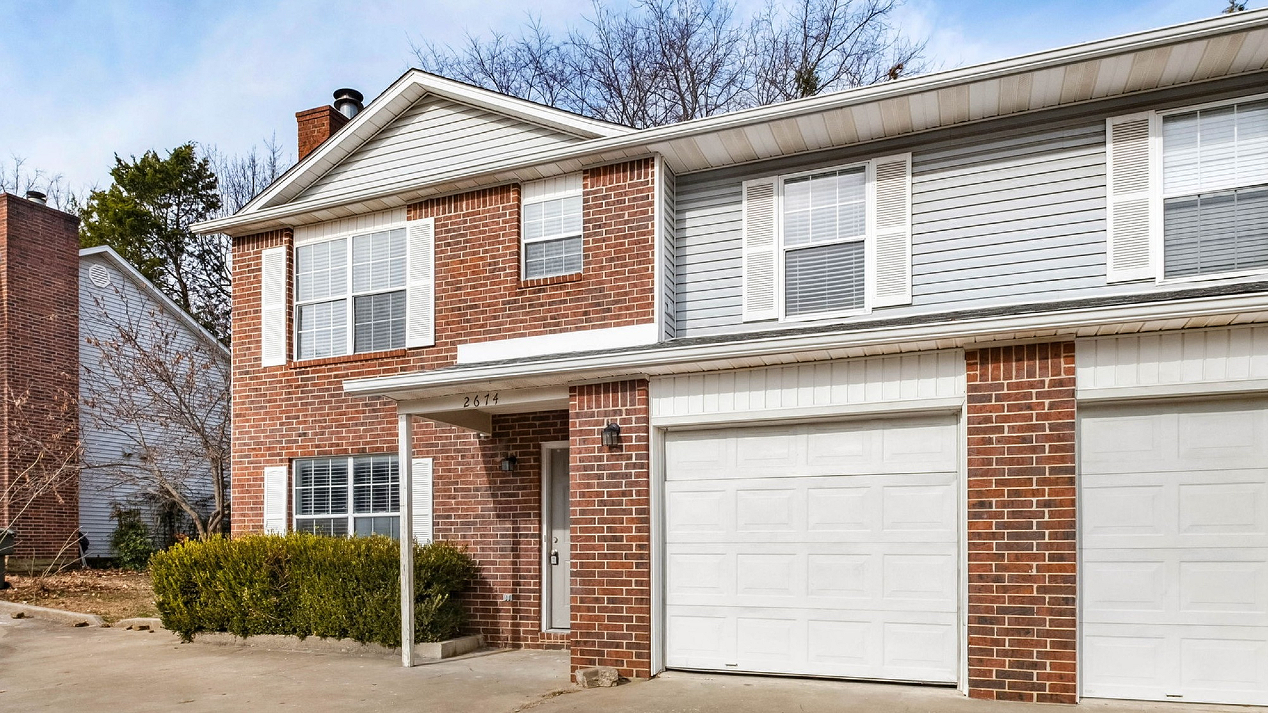 Charming red-brick townhouse with white accents and spacious double garage in a serene neighborhood setting.
