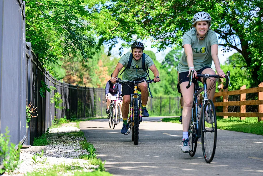 Joyful group of cyclists riding on a scenic path surrounded by lush greenery and vibrant trees on a sunny day.