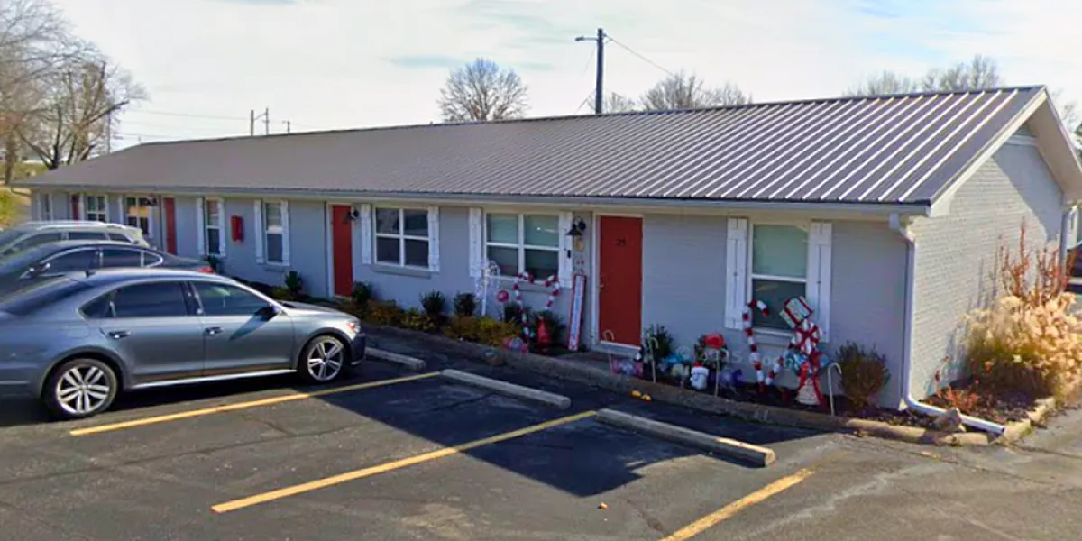Charming single-story apartment complex with stylish metal roofing, vibrant red doors, and thoughtful front garden decorations, offering convenient parking and a welcoming atmosphere.