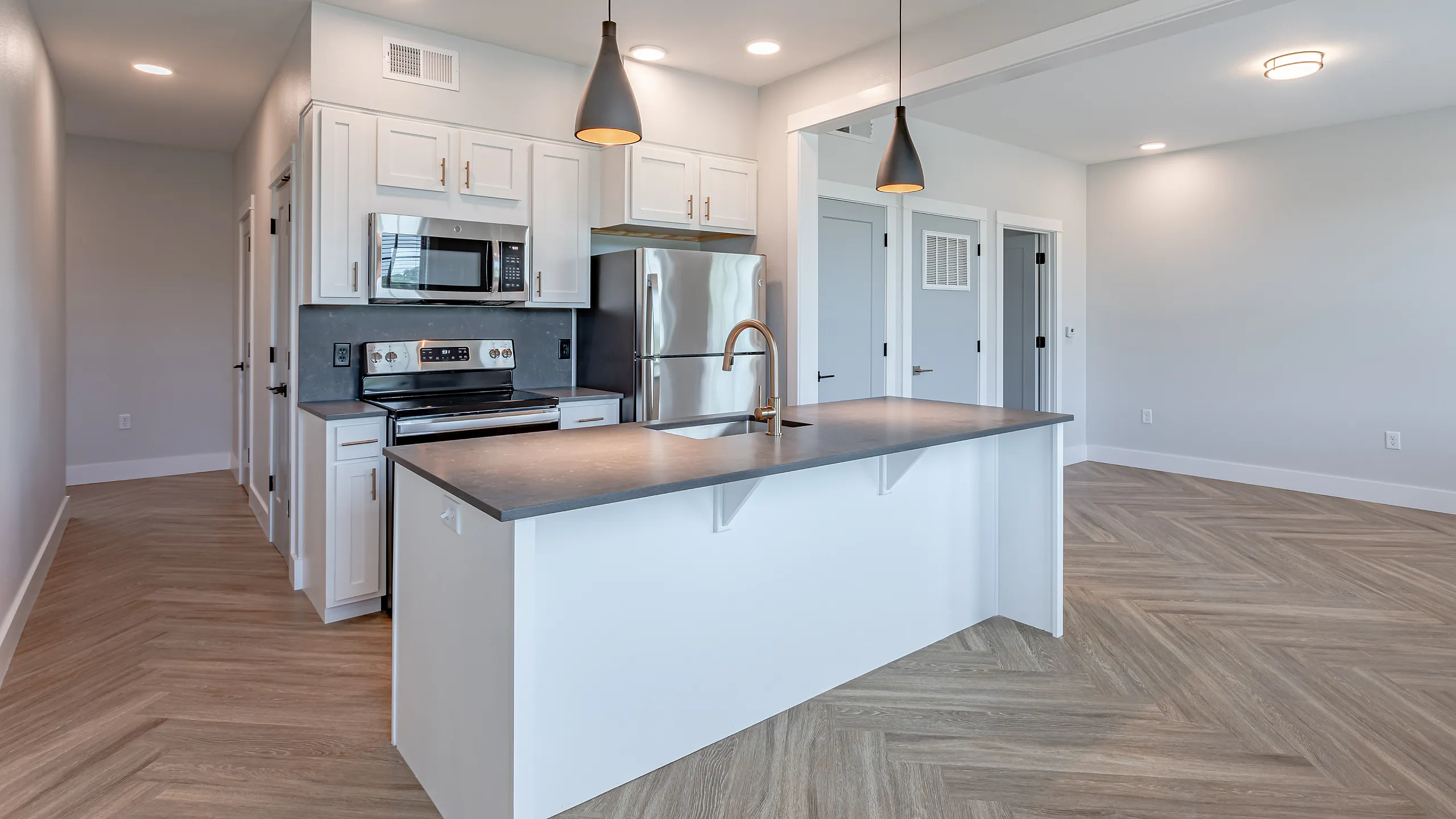 Modern apartment kitchen featuring sleek stainless steel appliances, elegant pendant lighting, and a spacious island with a stylish faucet.