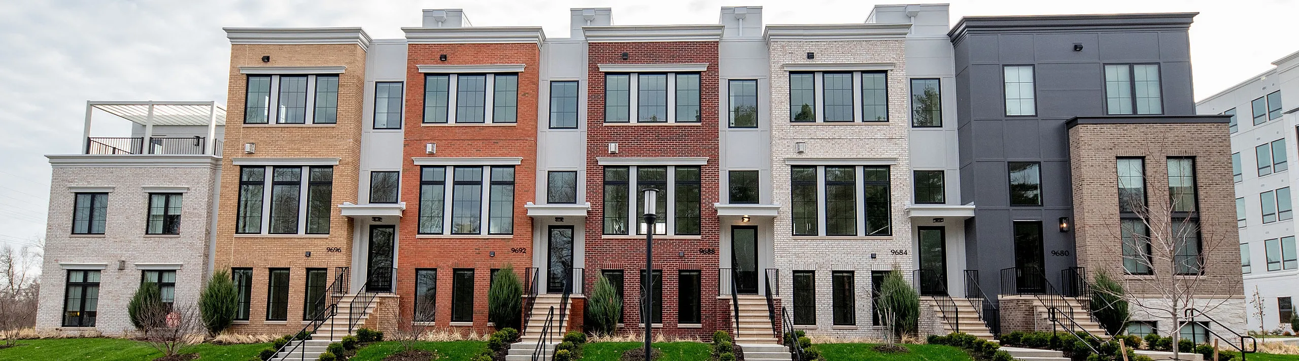 Chic modern row of townhomes with vibrant brick facades and large windows, set against a lush green landscape.