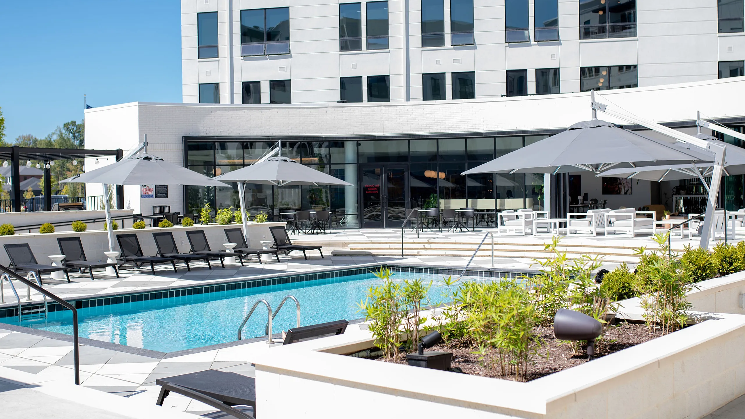 Modern apartment building with poolside loungers and shaded seating, featuring a bright and inviting outdoor area.