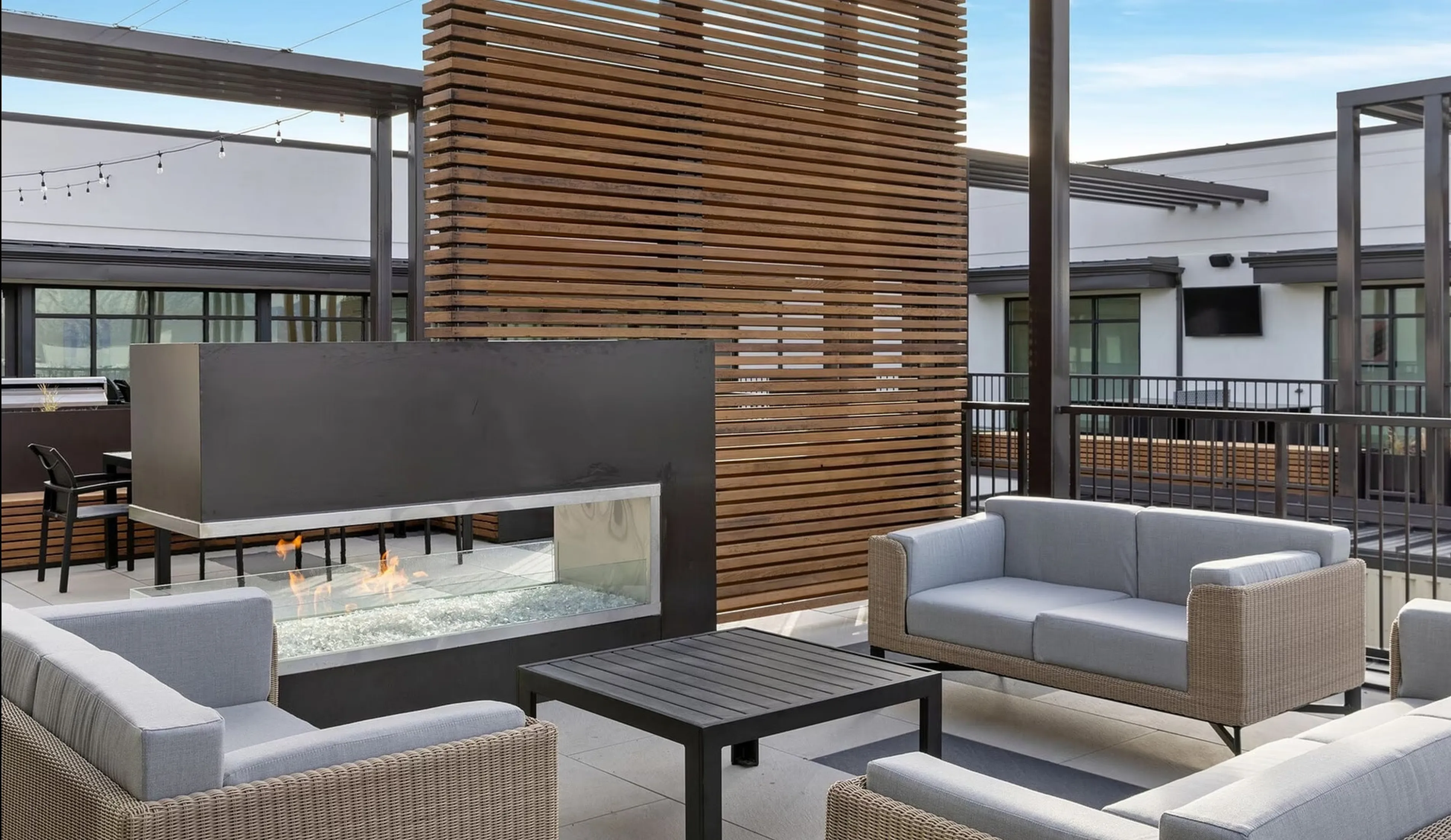 Modern rooftop lounge featuring cozy wicker seating around a sleek glass fireplace, perfect for outdoor relaxation.