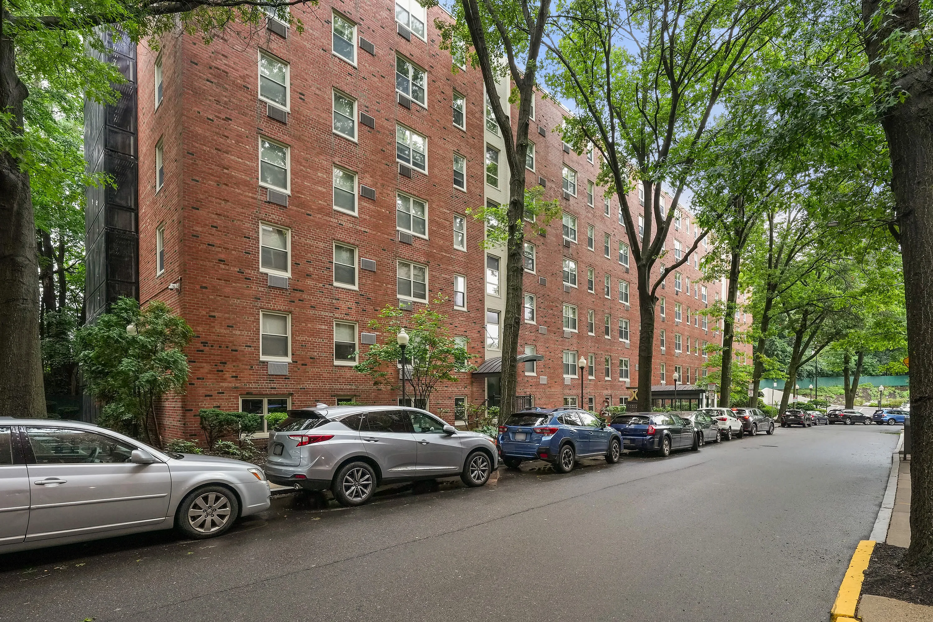 Charming brick apartment building nestled among lush trees, offering a serene urban living experience with convenient street parking.