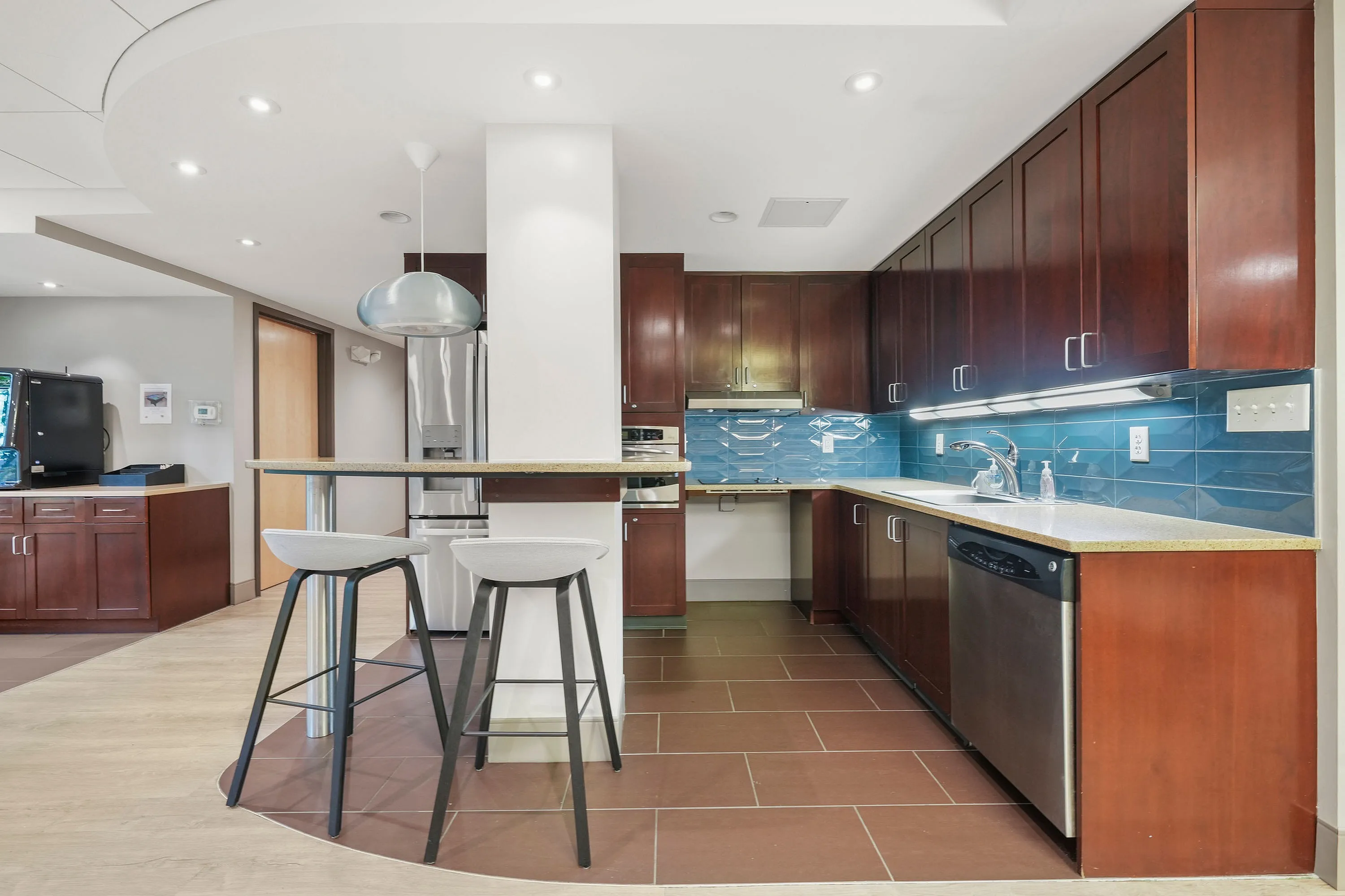 Sleek modern kitchen with rich wooden cabinetry, stainless steel appliances, blue tile backsplash, and stylish breakfast bar with chic seating.