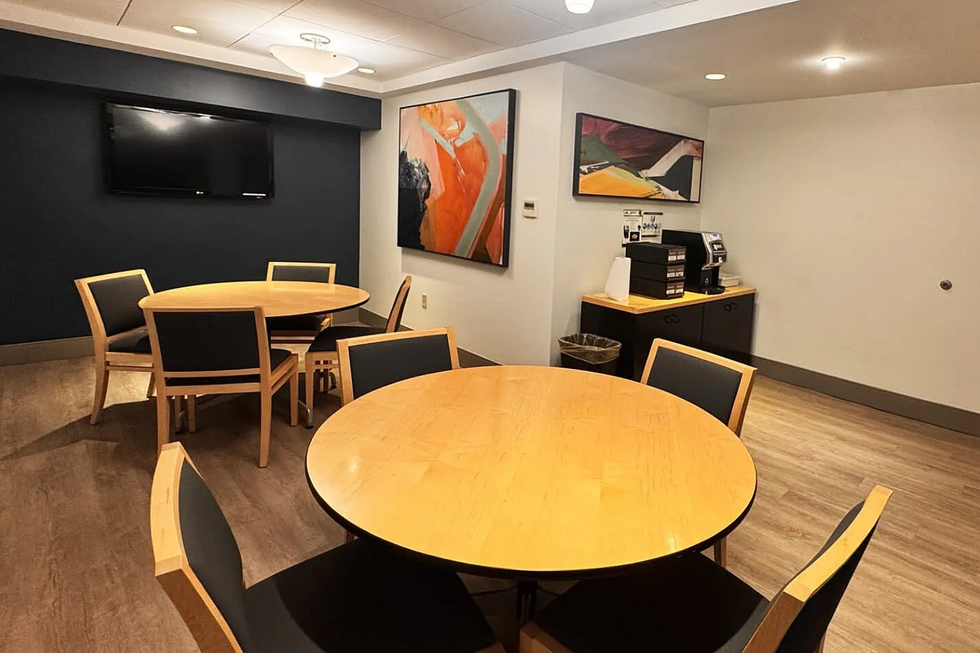 Modern communal dining area with elegant wooden tables, vibrant artwork, and an inviting coffee station.