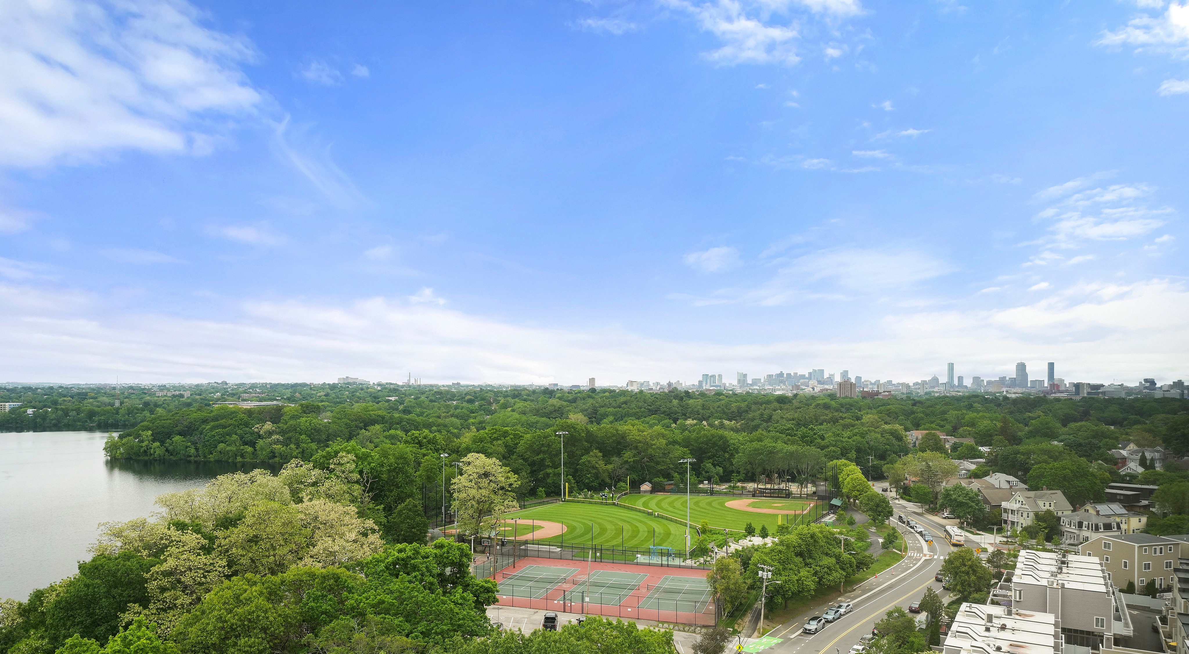 Breathtaking panoramic view of a vibrant cityscape with lush green parks, tennis courts, and a serene lake under a clear blue sky.