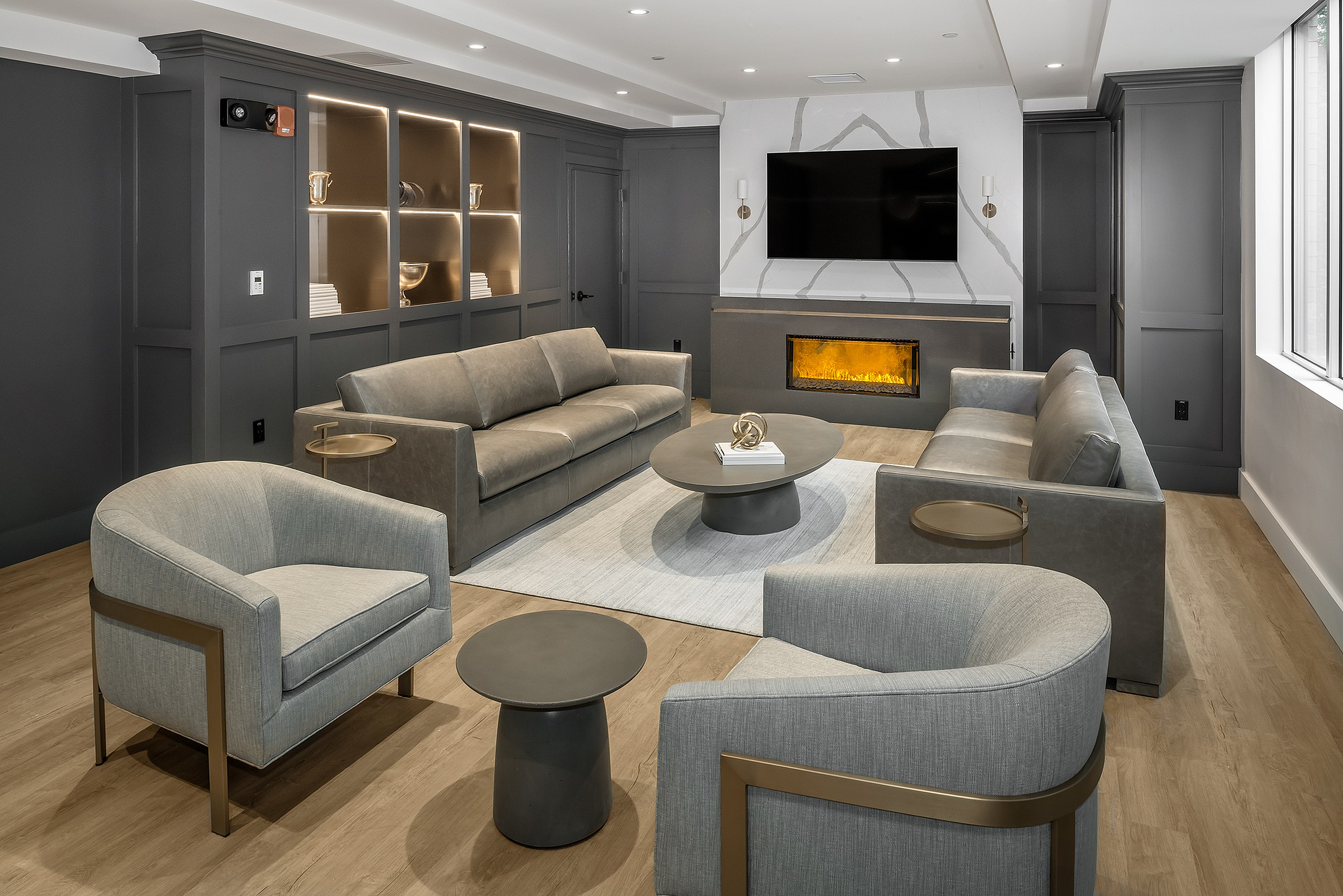 Luxurious modern living room with elegant gray sofas, sleek armchairs, and a cozy electric fireplace, bathed in natural light.