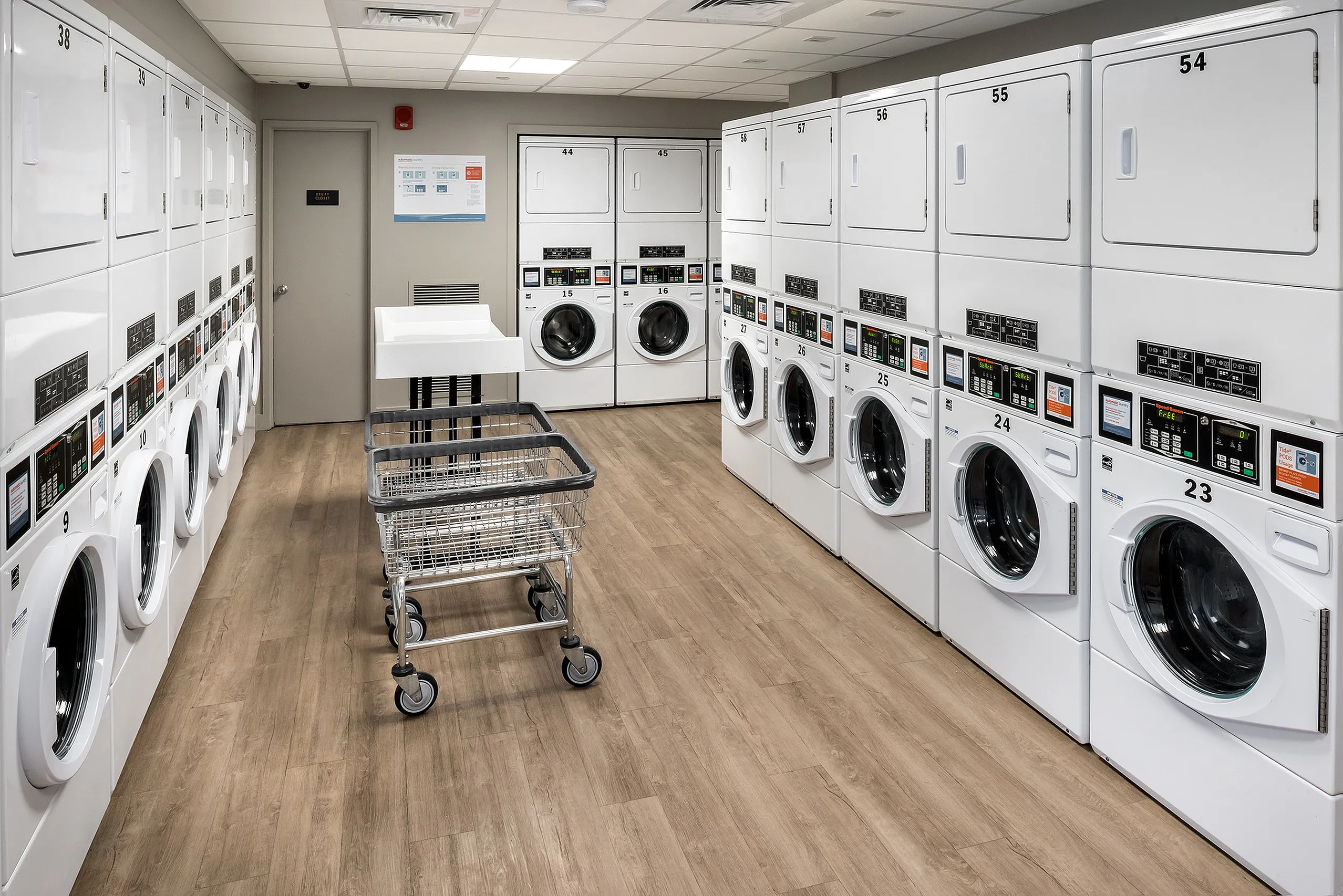Modern laundry facility with rows of sleek washers and dryers, featuring bright lighting and convenient rolling baskets.