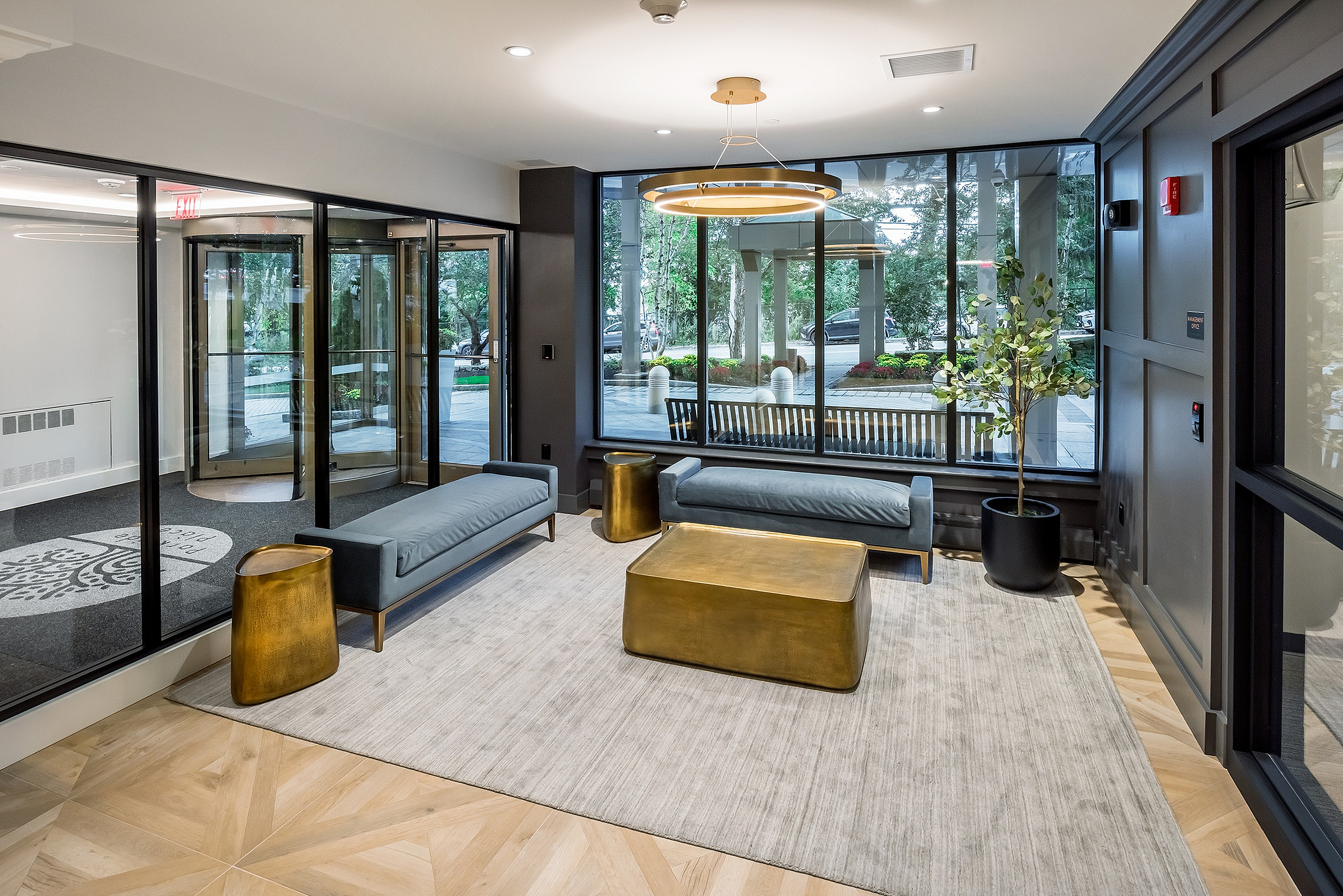 Chic apartment lobby with modern decor, featuring elegant gold accent tables, plush seating, and large windows with garden views.