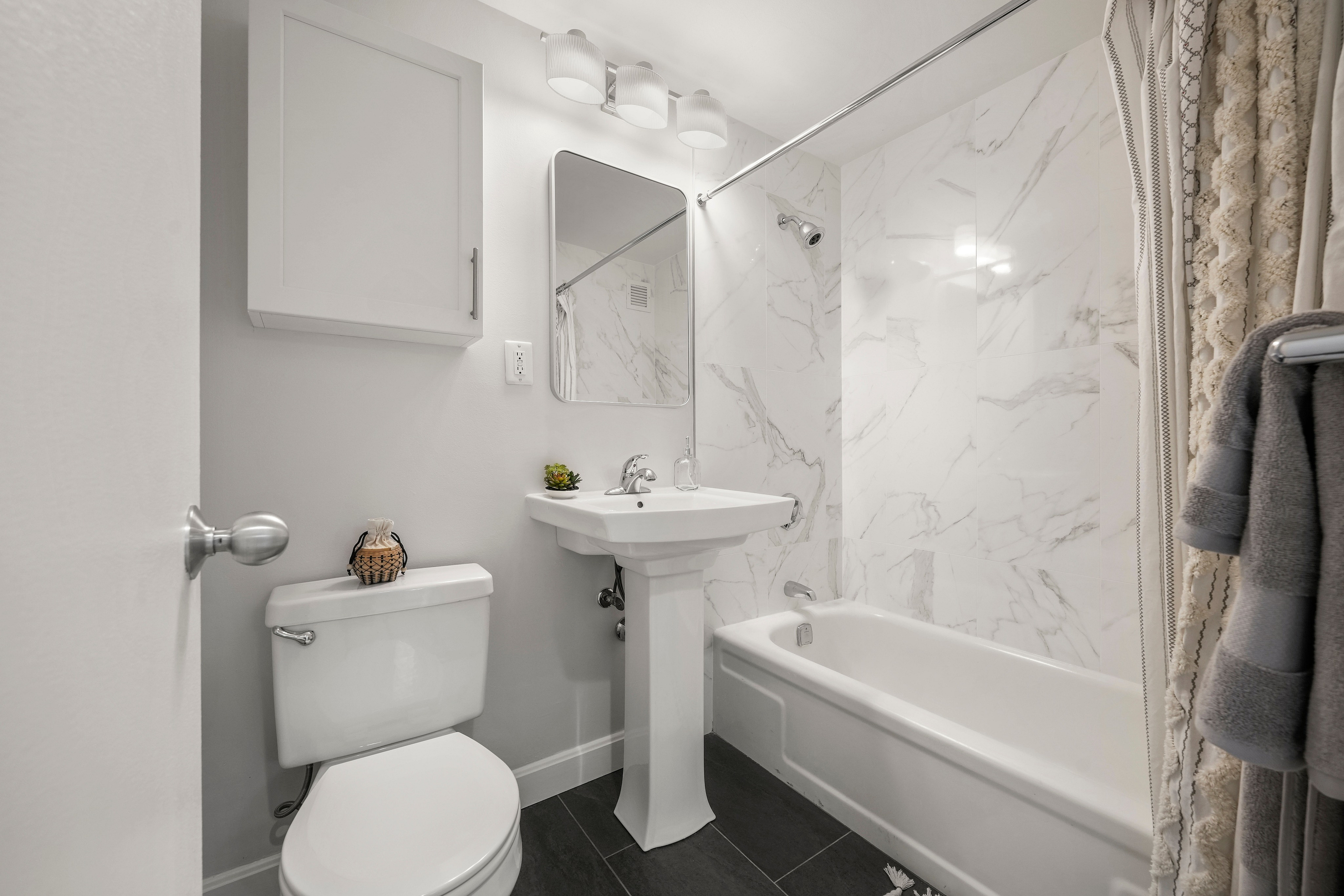 Elegant bathroom featuring a chic marble-tiled bathtub, modern pedestal sink, and soft lighting for a serene atmosphere.