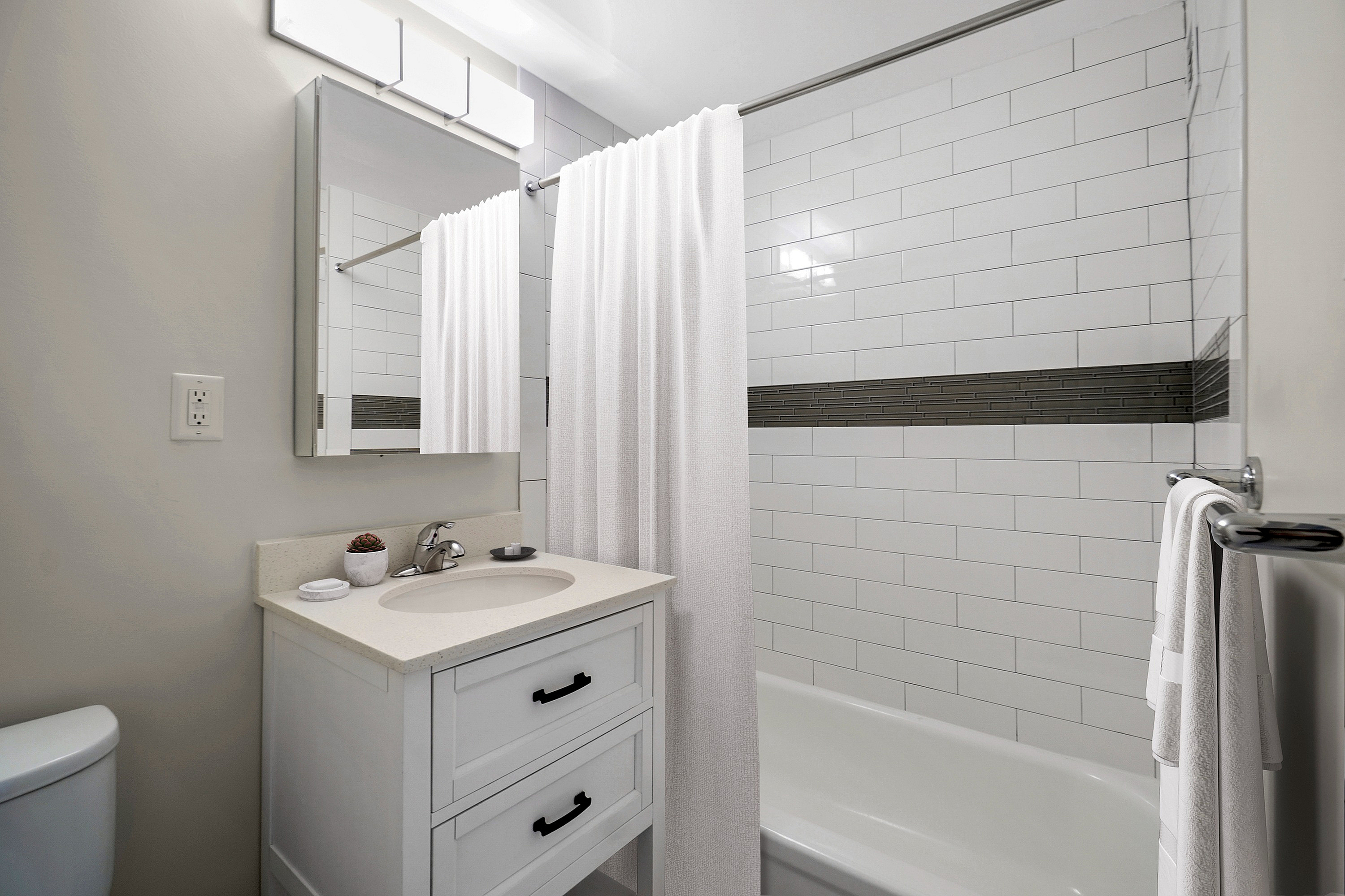 Elegant bathroom featuring a sleek white vanity, modern fixtures, and a pristine bathtub with classic tile accents.