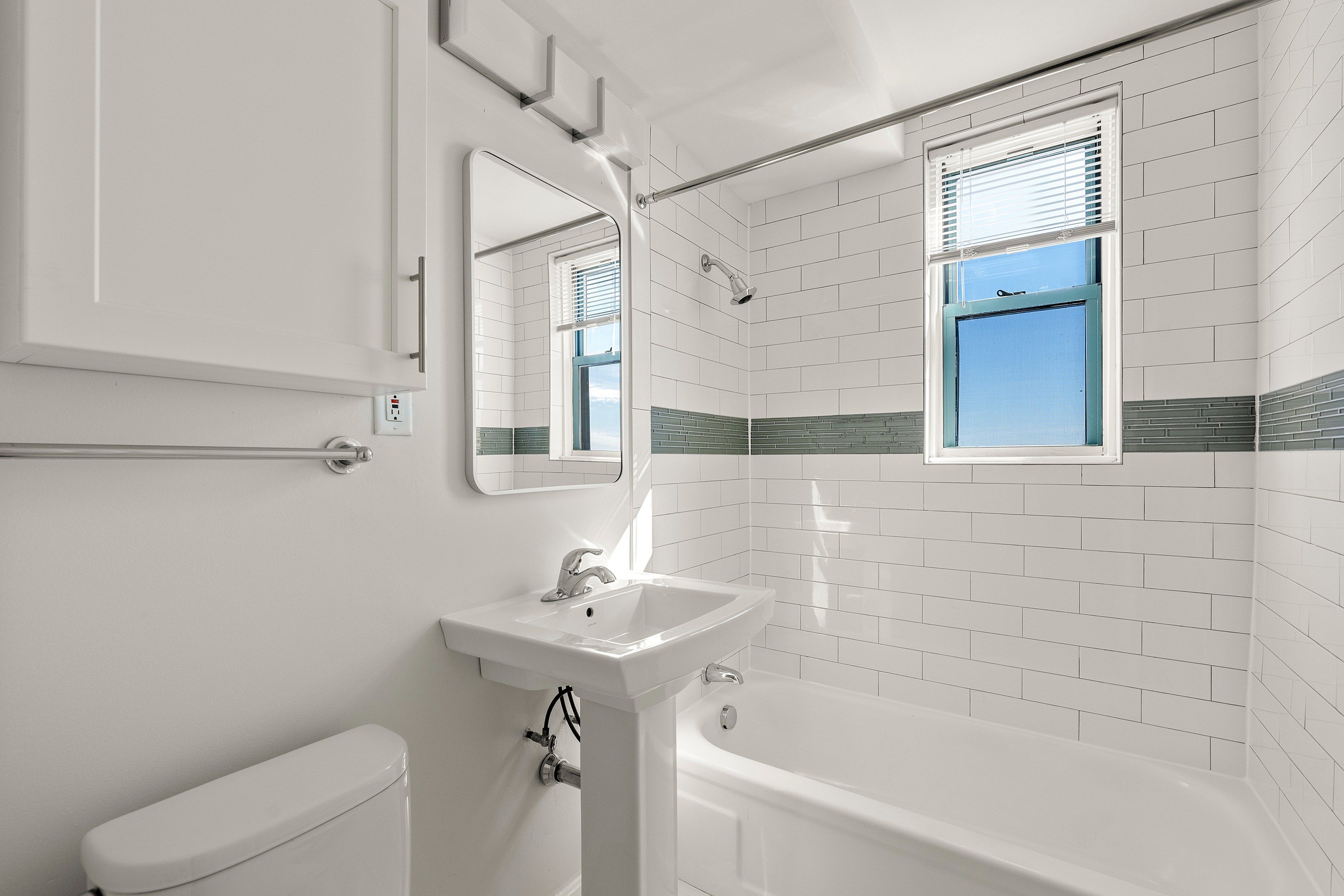 Bright and airy bathroom featuring modern white tiles, a sleek pedestal sink, and natural light through a large window.