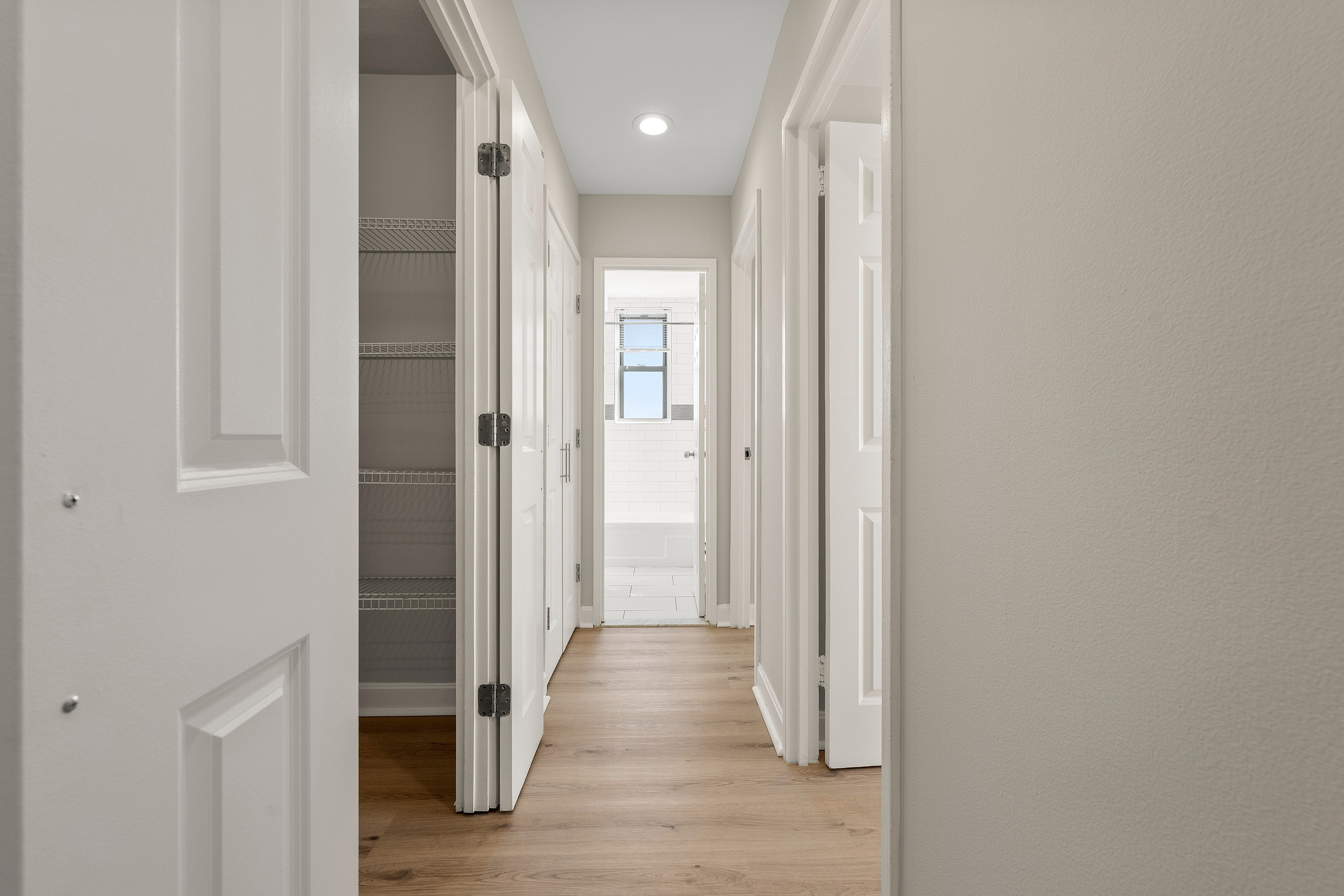 Bright hallway in a modern apartment with wood flooring and a view of a tiled bathroom at the end.