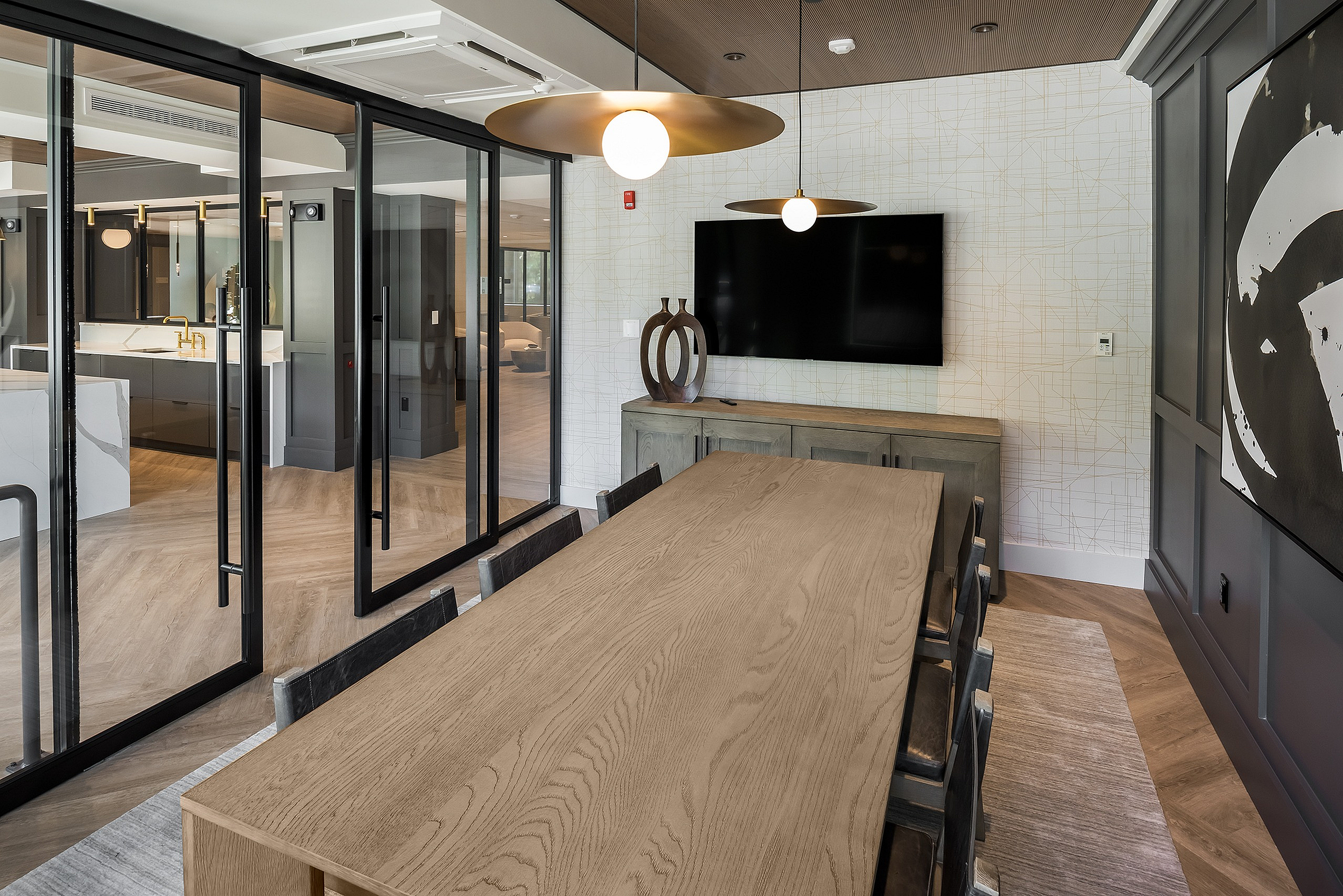 Elegant dining room with a modern wooden table, stylish pendant lighting, and floor-to-ceiling glass doors leading to a sleek kitchen area.