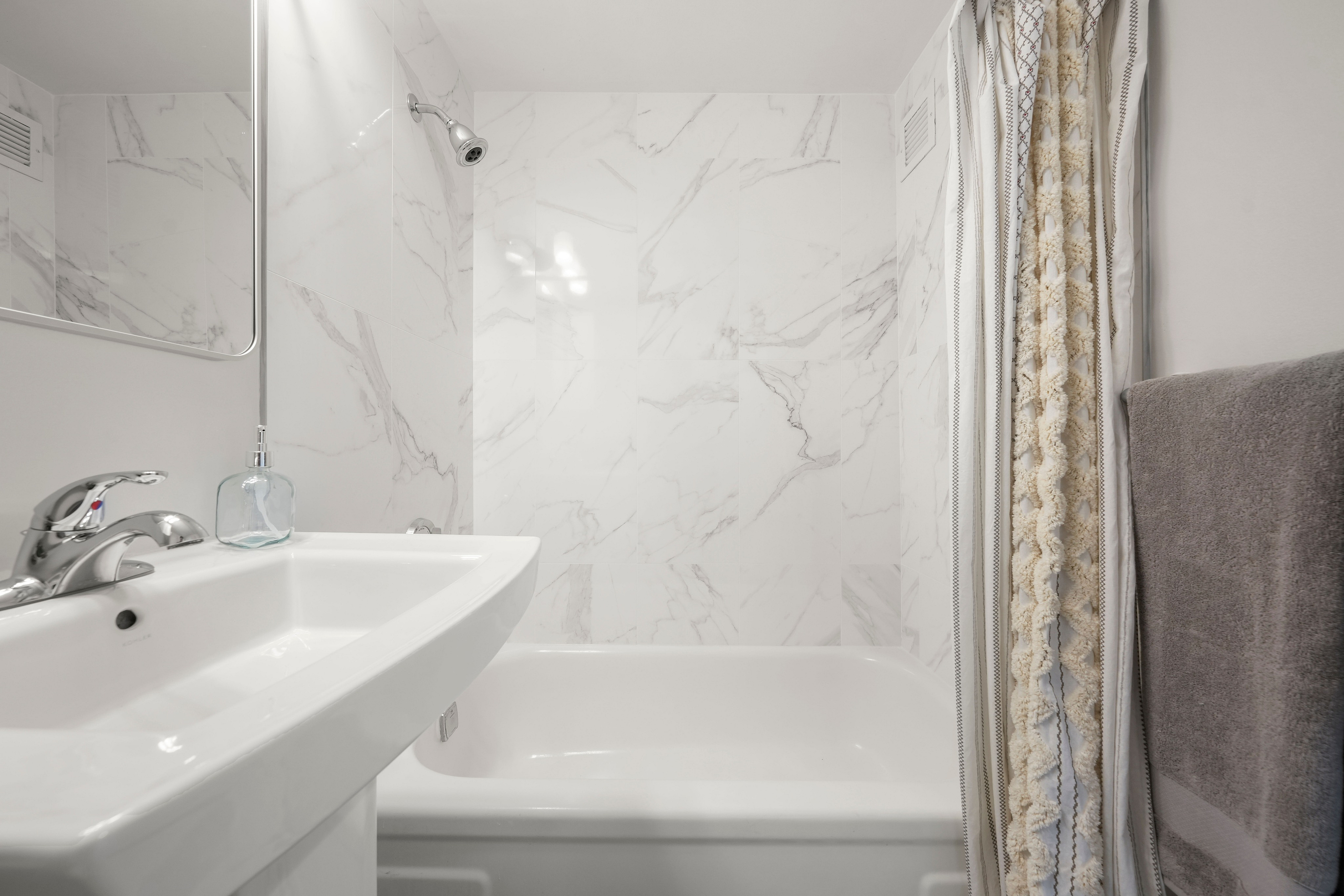 Elegant bathroom featuring marble tiles, a sleek white basin, and a cozy bathtub with artistic shower curtain.