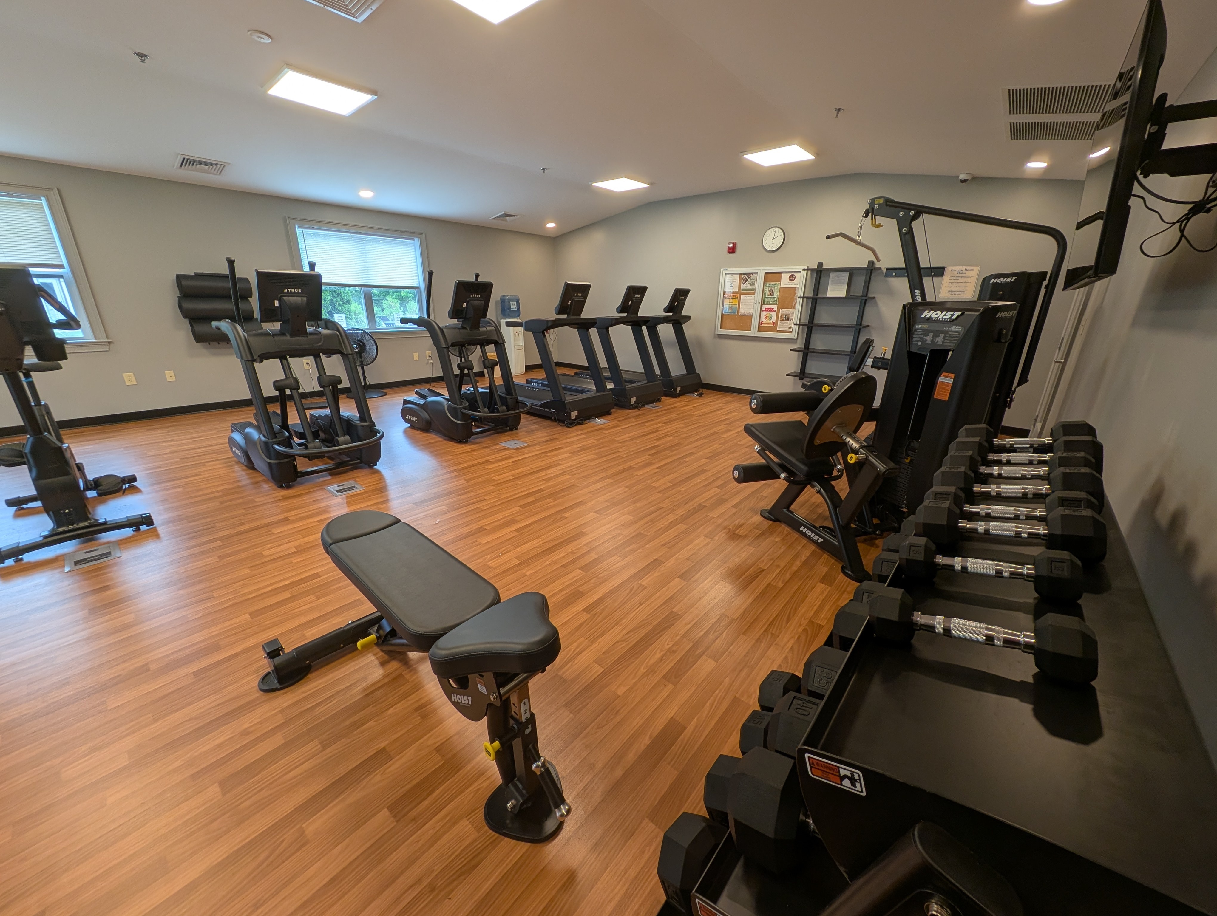 Modern fitness center with state-of-the-art treadmills, weight machines, and free weights, set on sleek wooden flooring.
