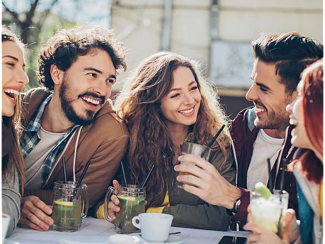 Joyful group of friends laughing and enjoying refreshing drinks at an outdoor cafe.