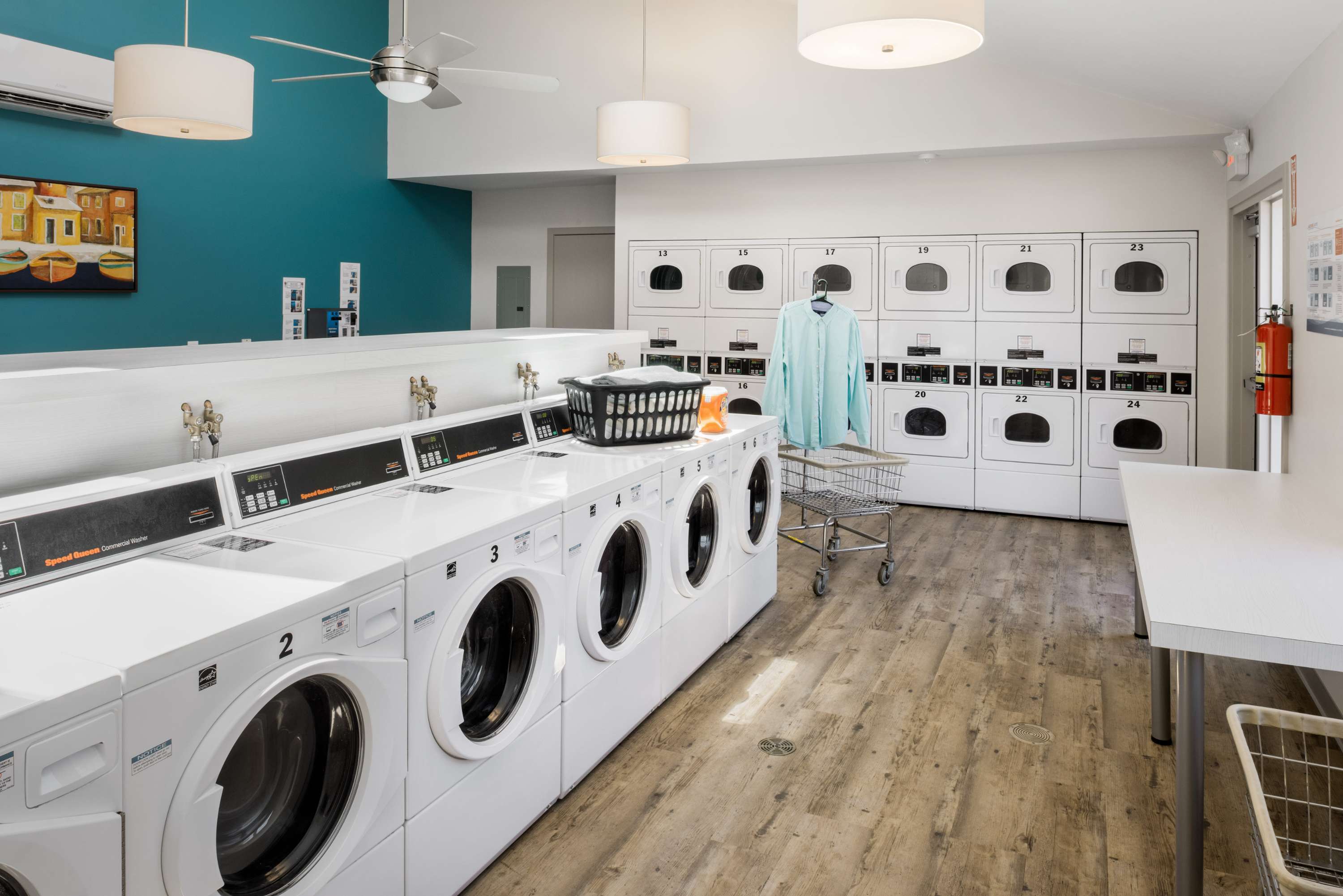 Modern and spacious laundry room with energy-efficient washers and dryers, vibrant teal accent wall, and ample folding space for convenience.